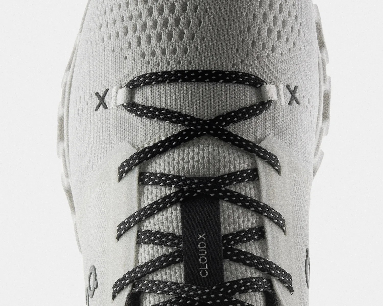 Close-up of white sneaker with black and white speckled laces and "CLOUD X" text on the tongue.