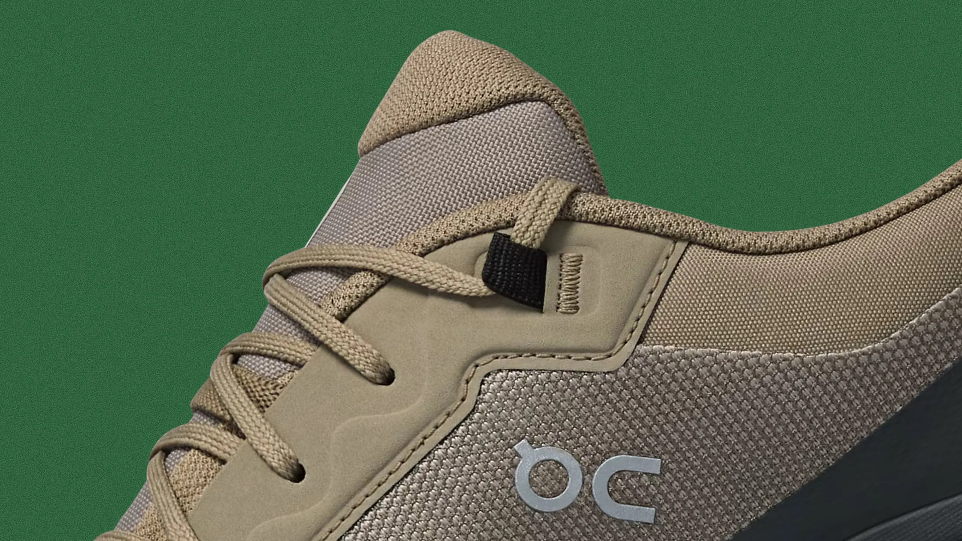 Close-up of a beige and taupe sneaker with textured fabric and beige laces on a green background.