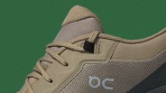 Close-up of a beige and taupe sneaker with textured fabric and beige laces on a green background.