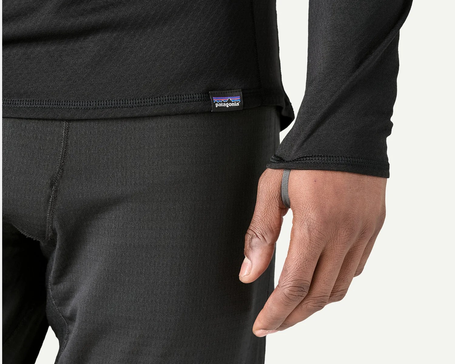 Close-up of a person wearing black Patagonia thermal base layer pants and top with thumb loop on the sleeve.