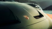 Close-up of a metallic green Porsche hood with the Porsche emblem and air vents.