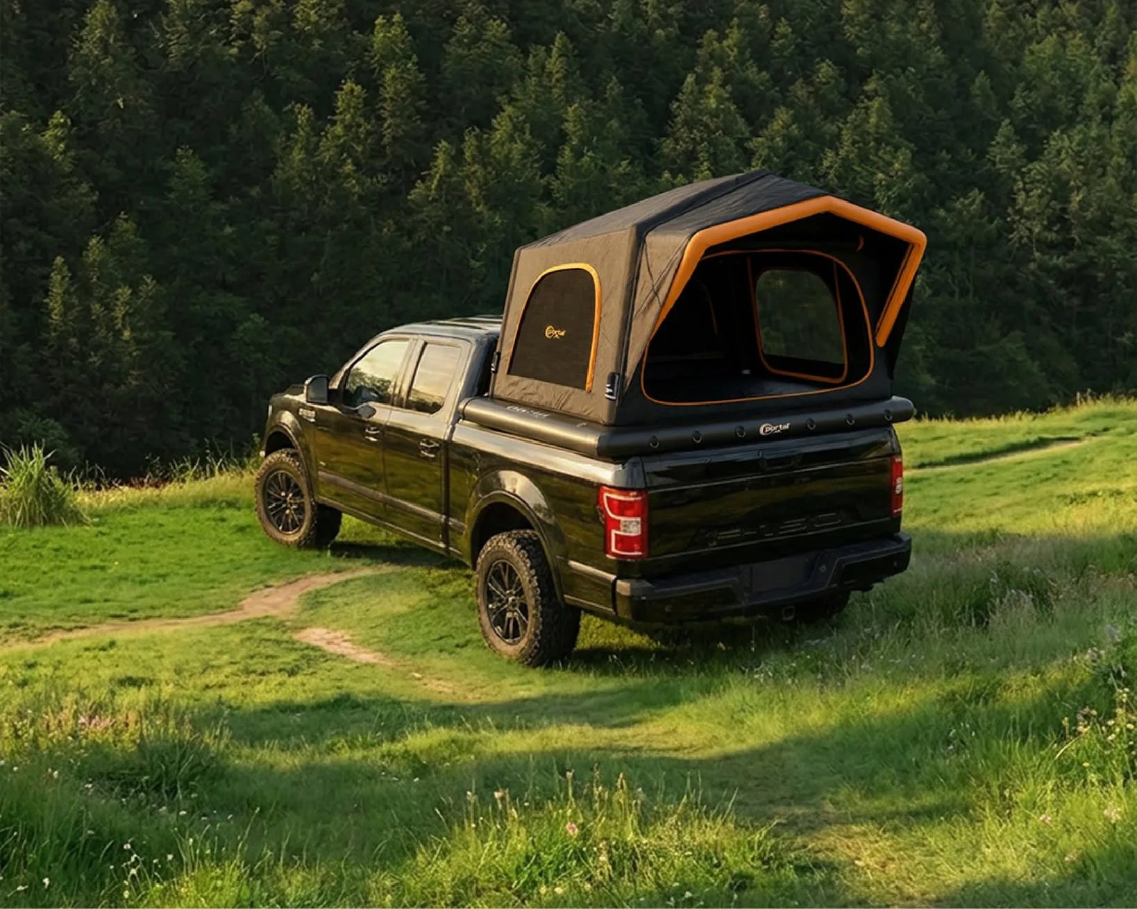 Black pickup truck with an orange-trimmed rooftop tent mounted on the bed, parked on a grassy hill near a forest.