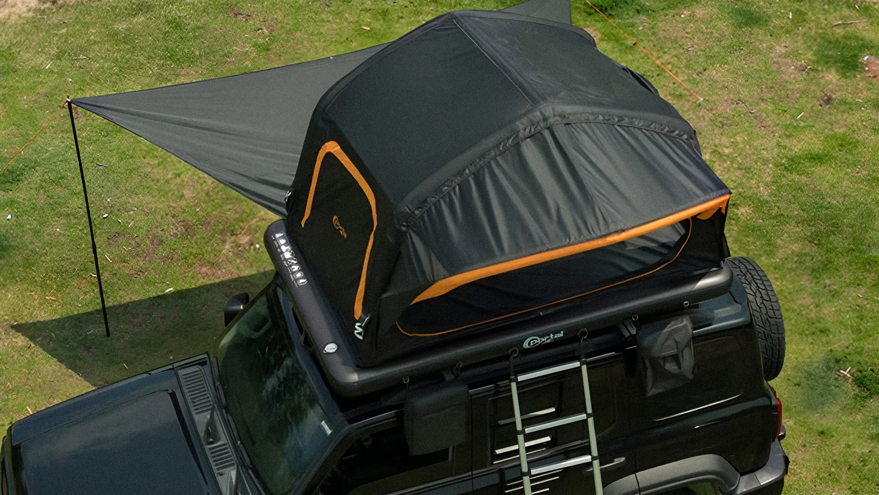 Black rooftop tent with orange trim mounted on a black SUV with an extended awning.