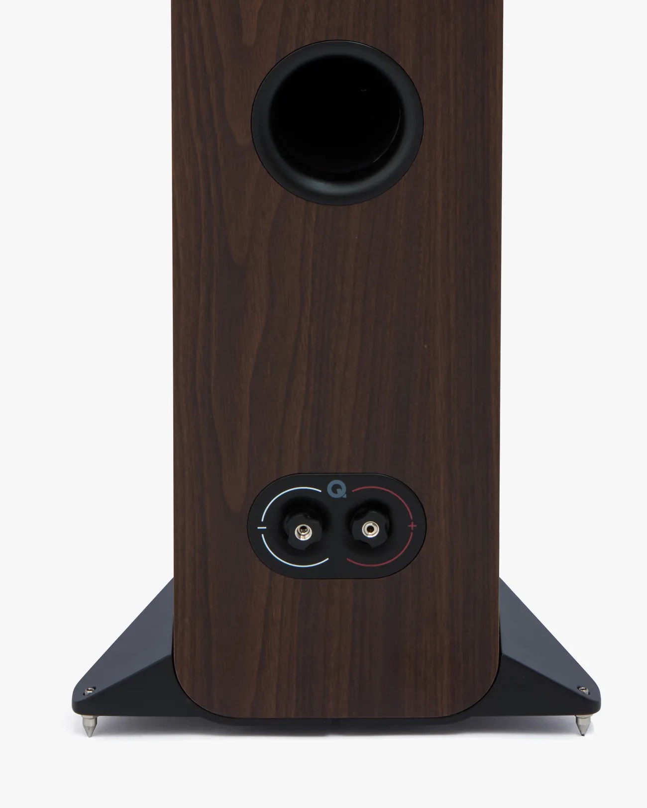 Rear view of a dark wood-finished speaker with a circular port and two speaker wire terminals on a black base with metal spikes.
