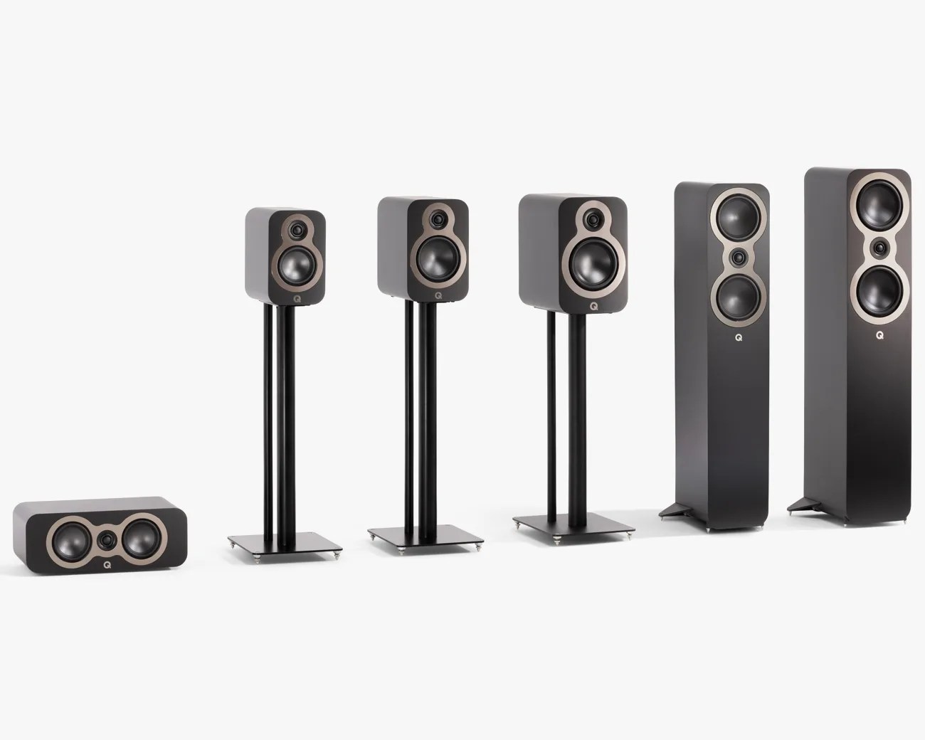Six black Q Acoustics speakers of varying sizes, including two floor-standing, three bookshelf on stands, and one horizontal center speaker.