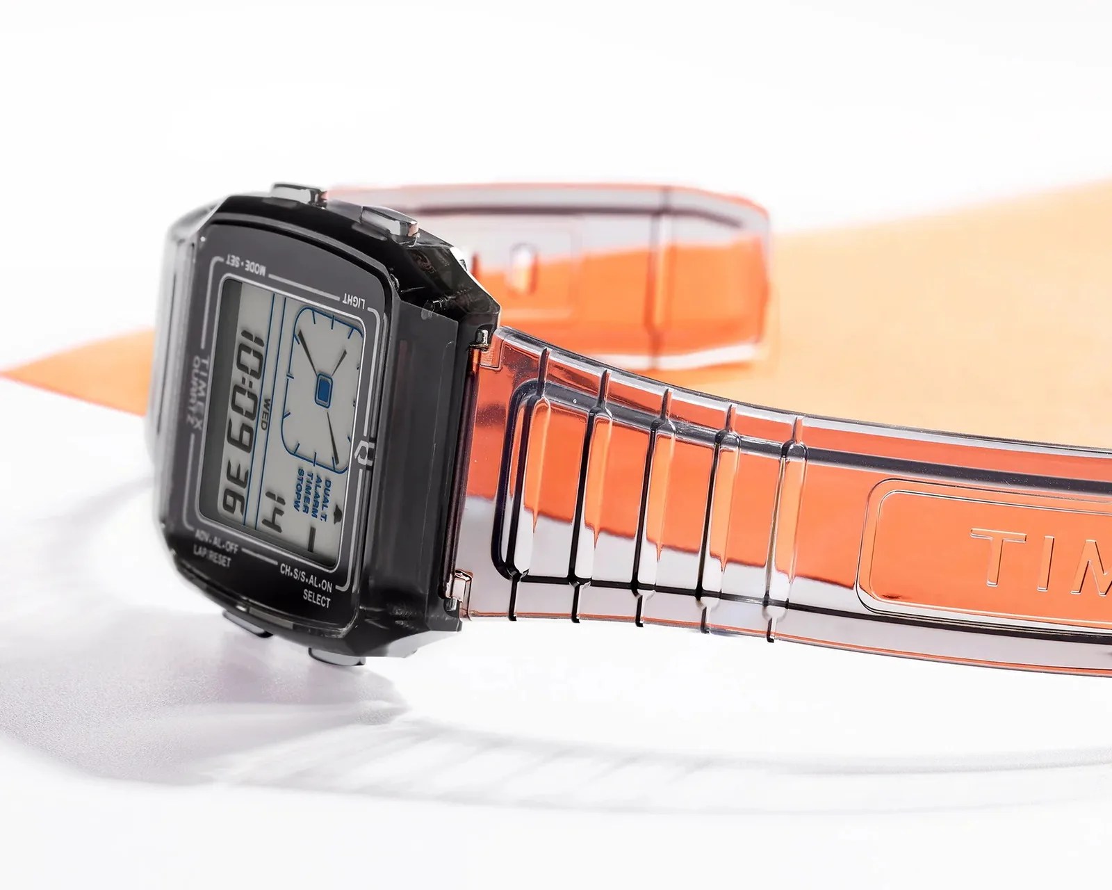Digital wristwatch with a black rectangular face and translucent orange plastic strap.