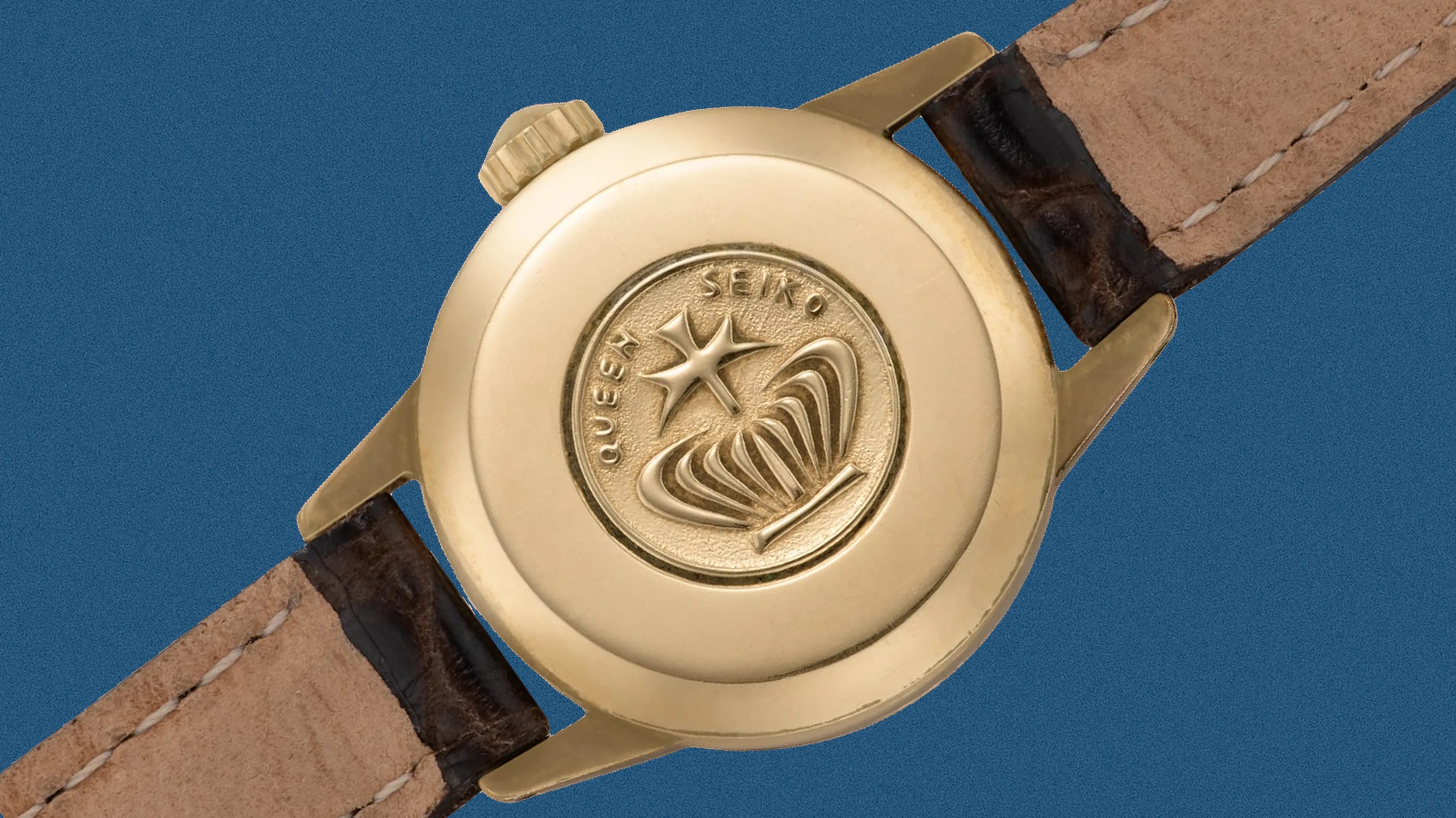 Gold watch case back with embossed "Queen Seiko" logo and brown leather strap.