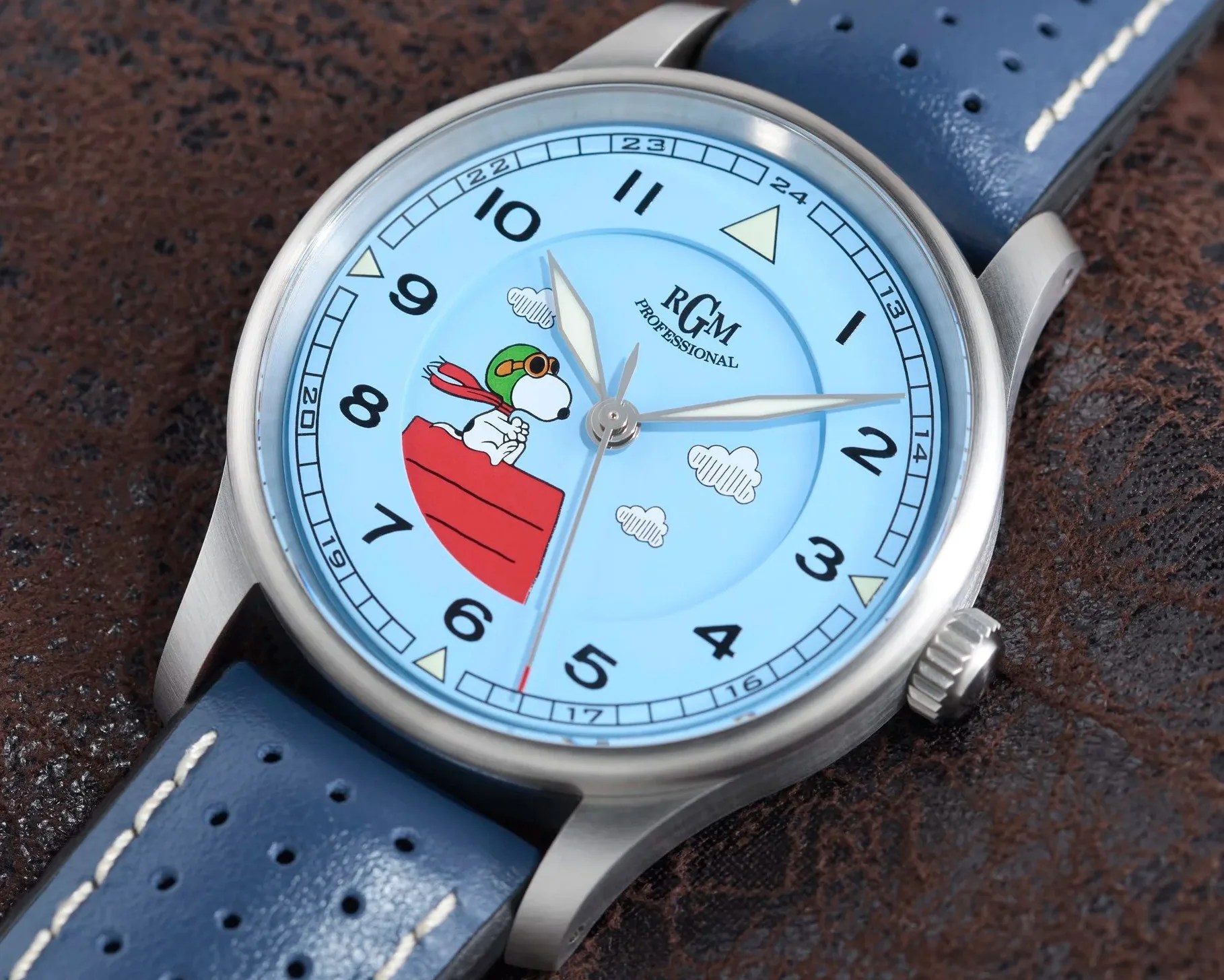 Close-up of a wristwatch with a light blue dial featuring Snoopy in aviator gear on a red doghouse, black numerals, and a blue perforated leather strap.