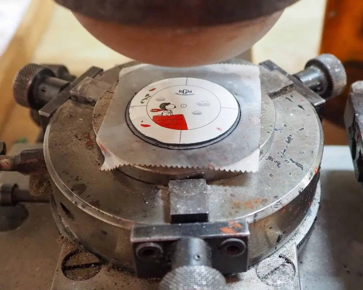Close-up of a round metal engraving or printing plate with a Snoopy illustration on a mechanical device.