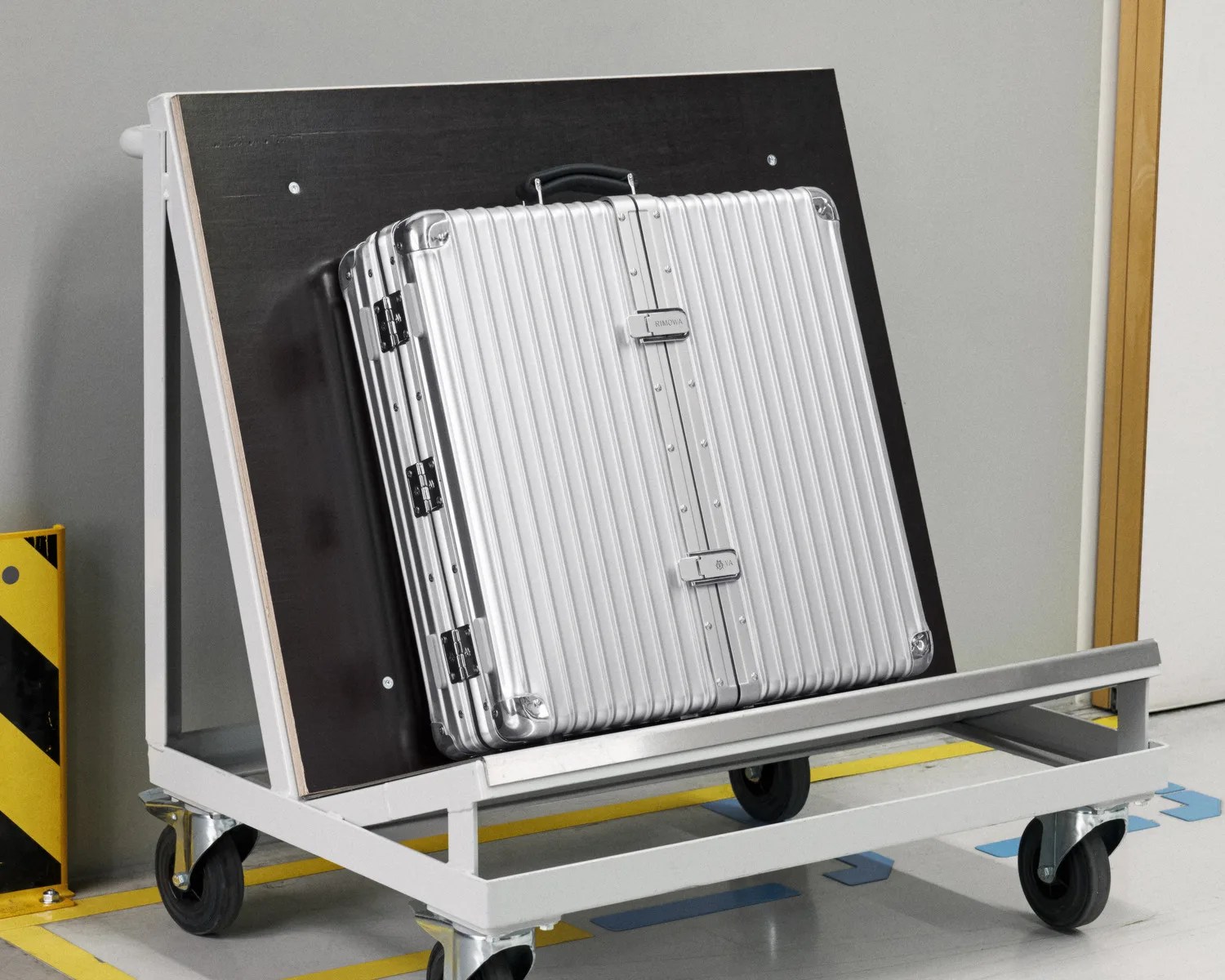 Silver hard-shell suitcase with vertical ridges and black handle on a gray metal cart with wheels.