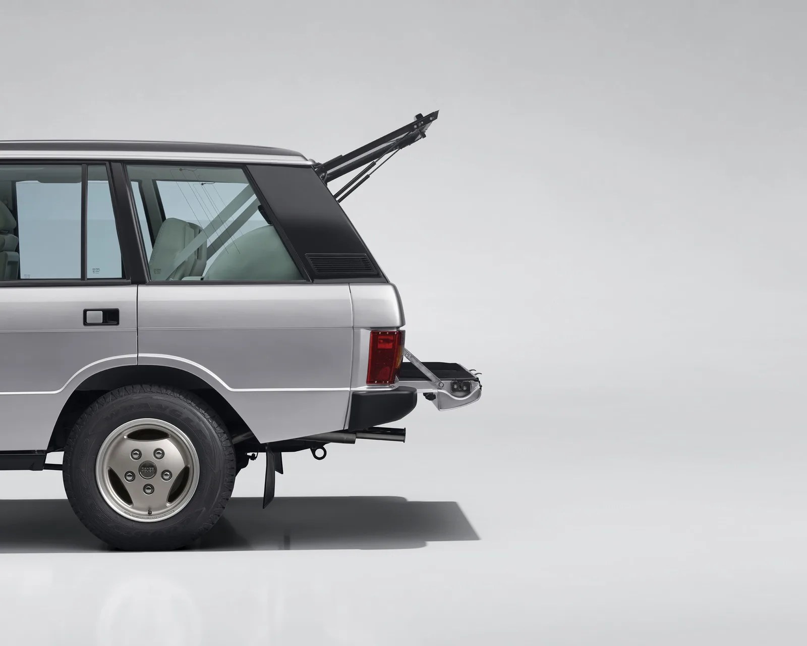 Silver SUV rear side with open tailgate and tailgate-mounted metal tray on a plain background.