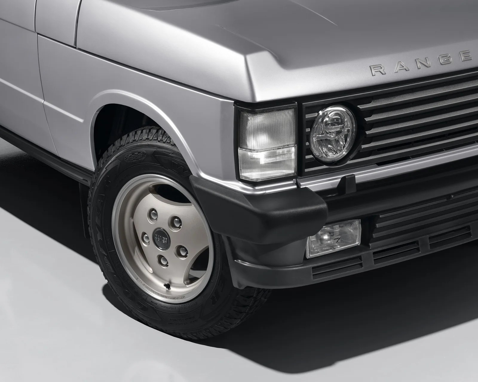 Close-up of silver Range Rover front left wheel, headlight, and black bumper on a gray floor.