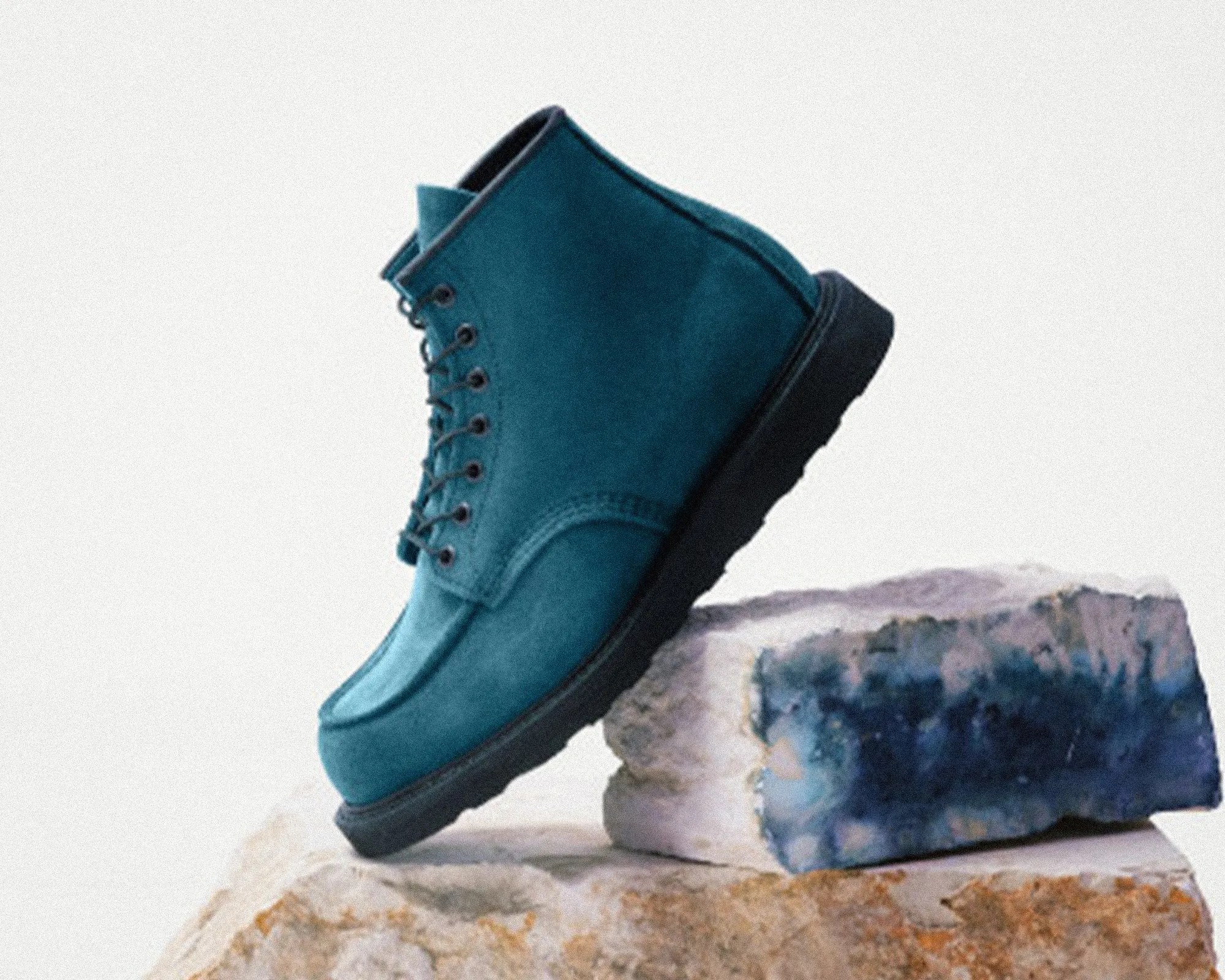 Teal suede lace-up boot with black sole resting on blue and beige geode stones.