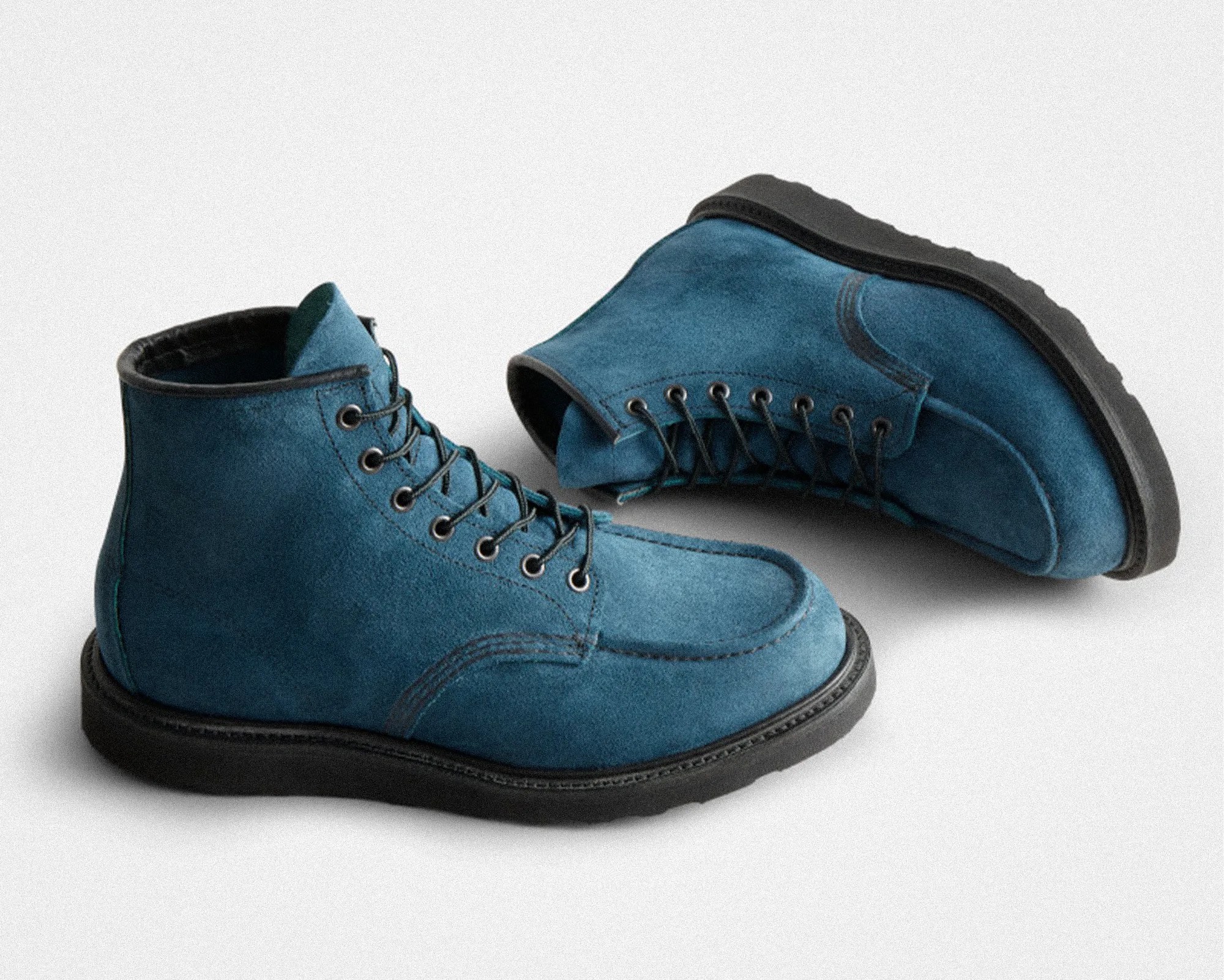 Pair of blue suede lace-up boots with black soles on a white background.