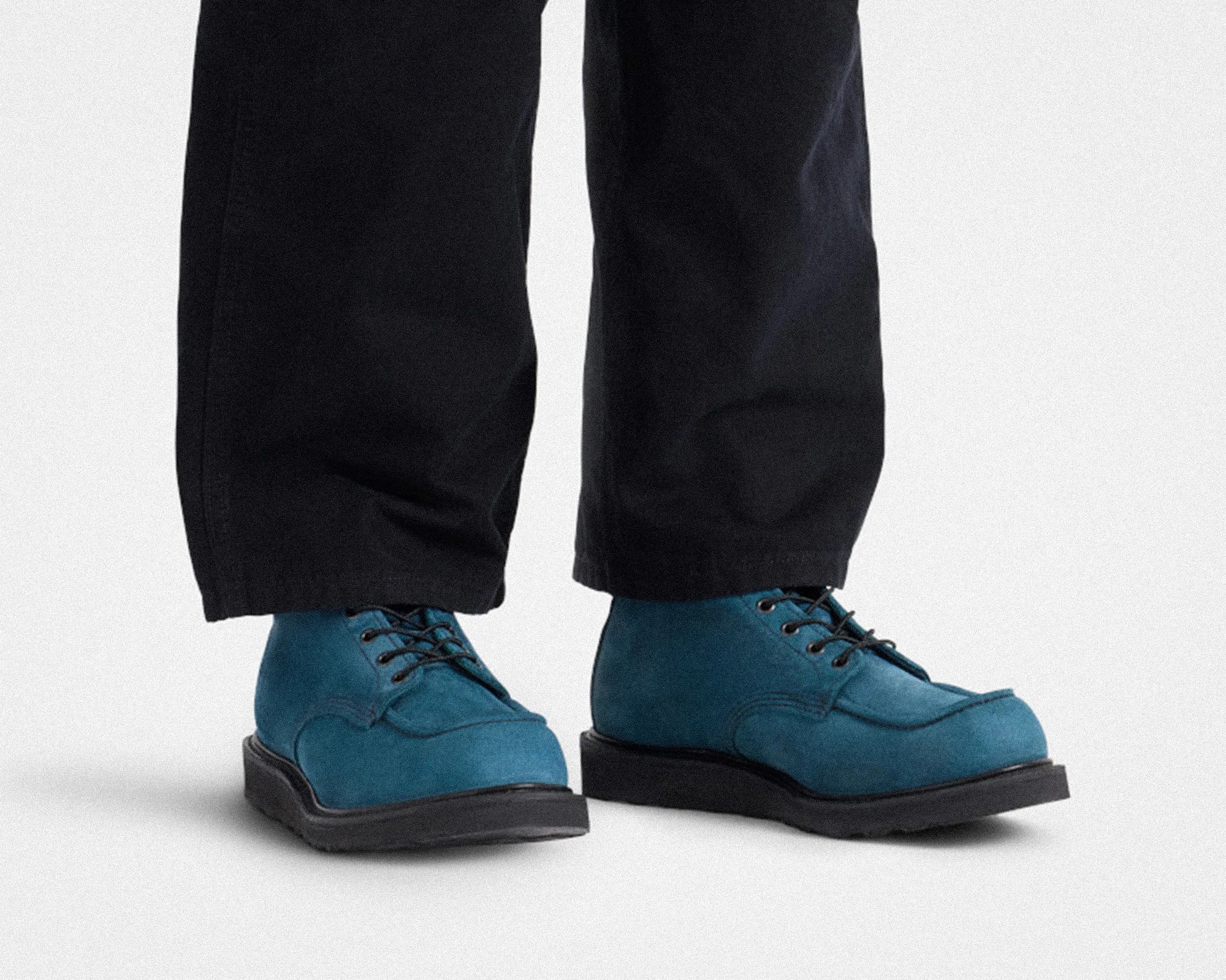 Blue suede lace-up boots with black soles worn with black pants.