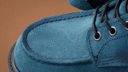 Close-up of blue suede shoe with black laces and brown stitching on a brown background.