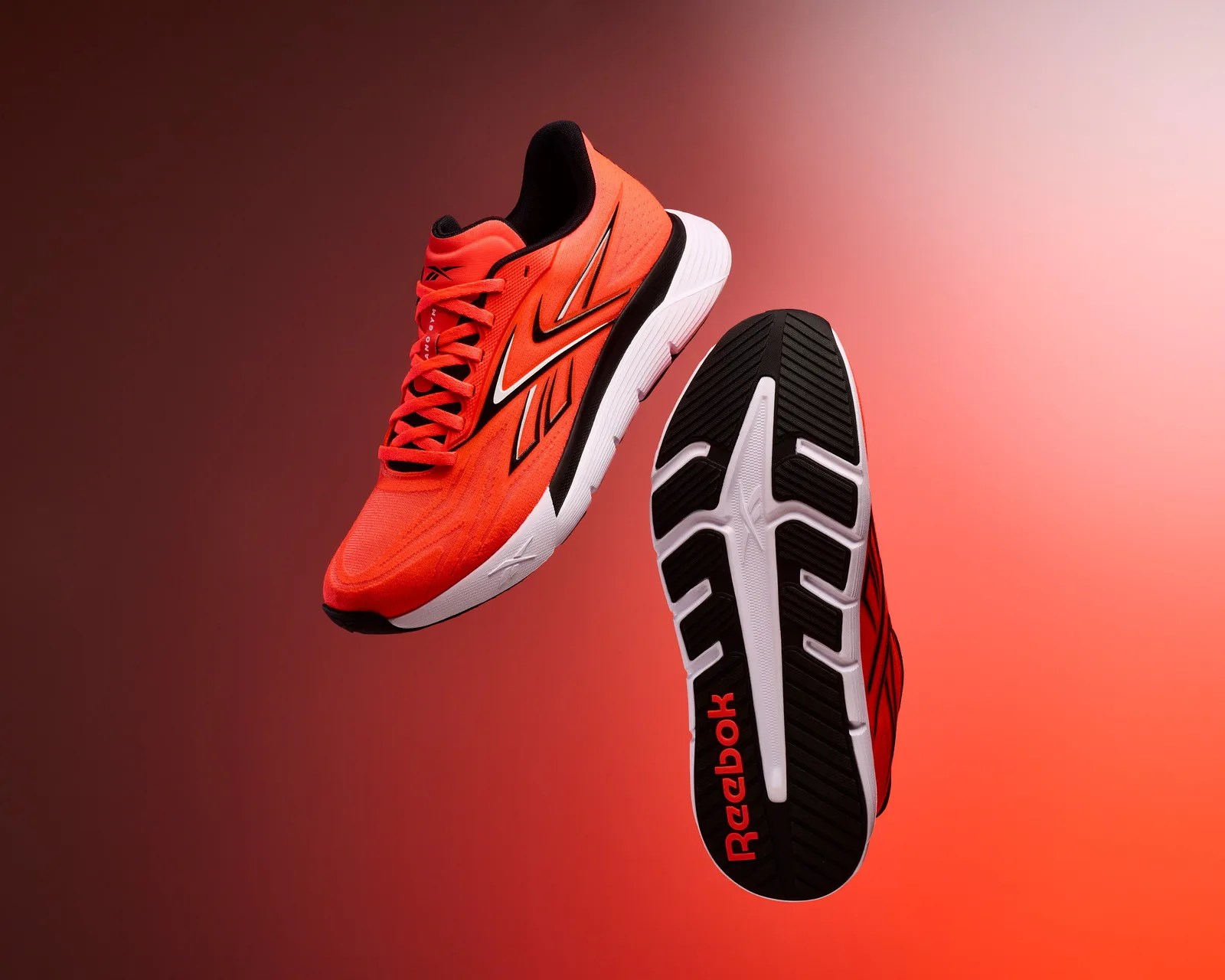 Bright orange Reebok running shoes with black and white soles against a gradient red background.