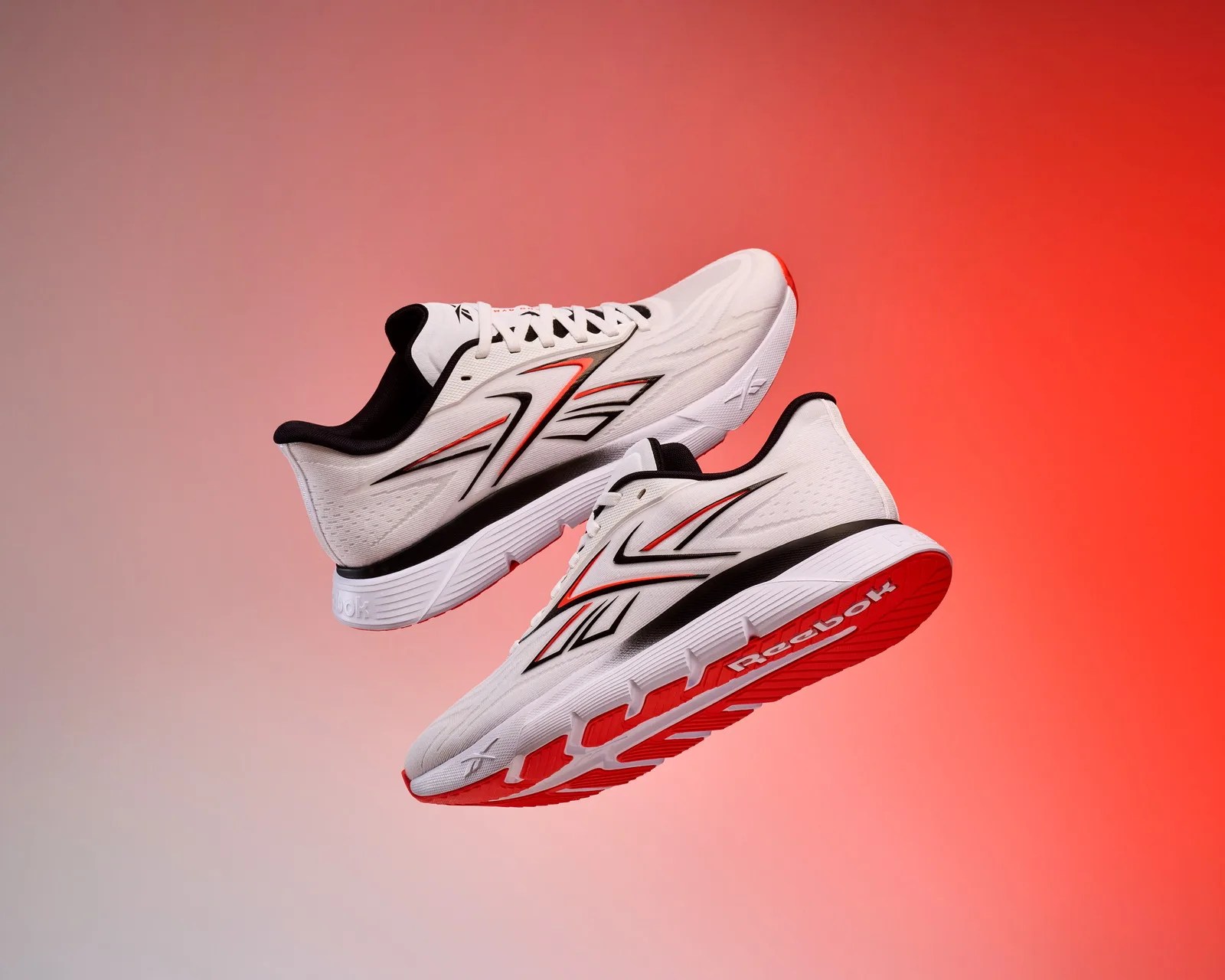 Pair of white Reebok running shoes with black and red accents floating against a red gradient background.