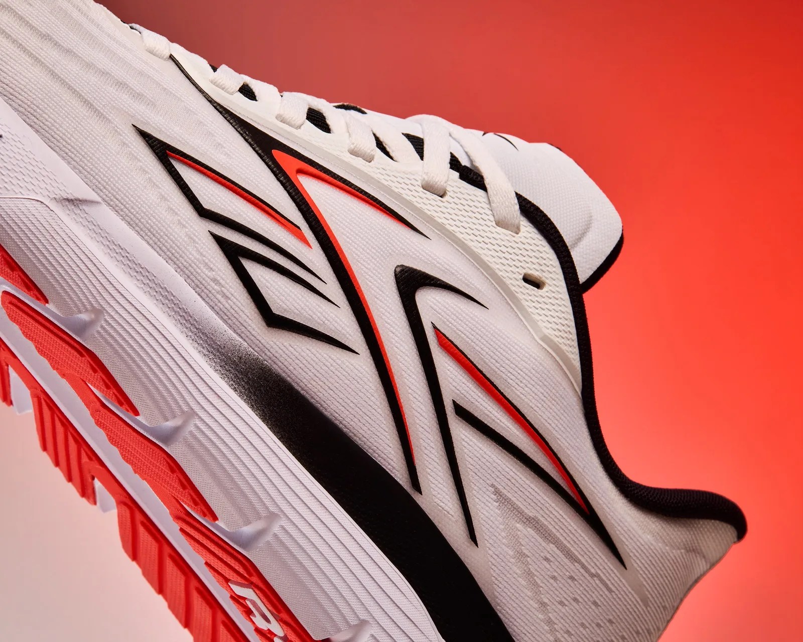 White running shoe with black and red geometric accents and red tread on a red background.
