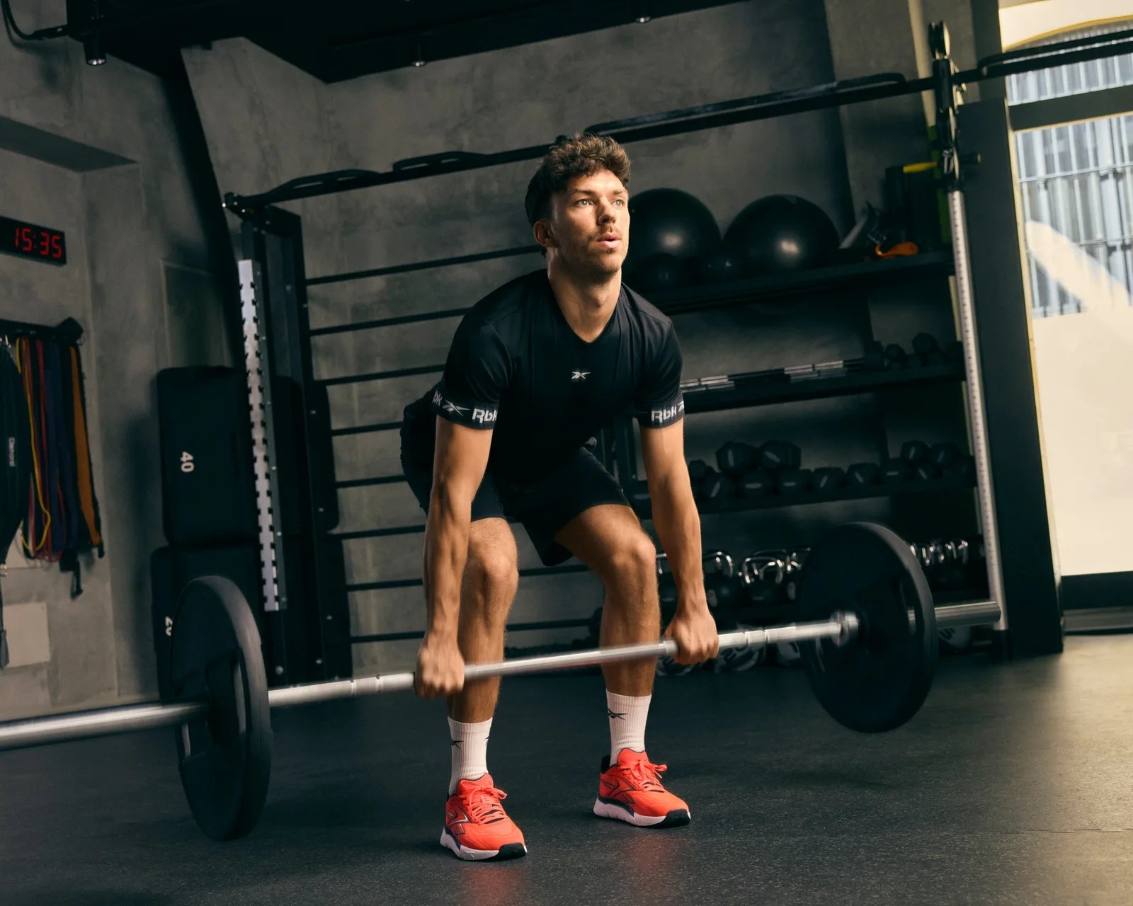 Man in black athletic outfit lifting a barbell with black weight plates in a gym.