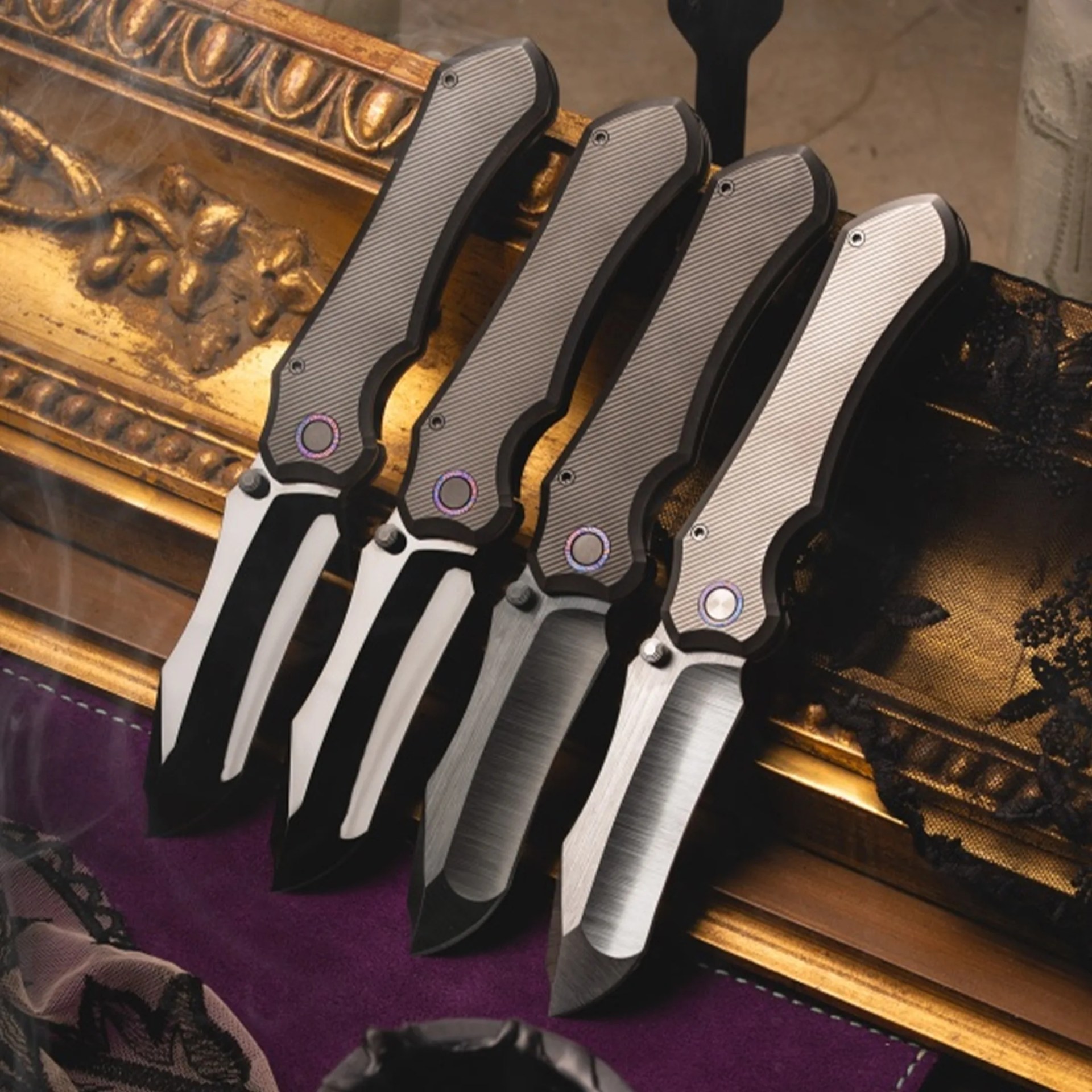 Four folding knives with textured gray handles and partially serrated blades arranged on a purple fabric and ornate gold surface.
