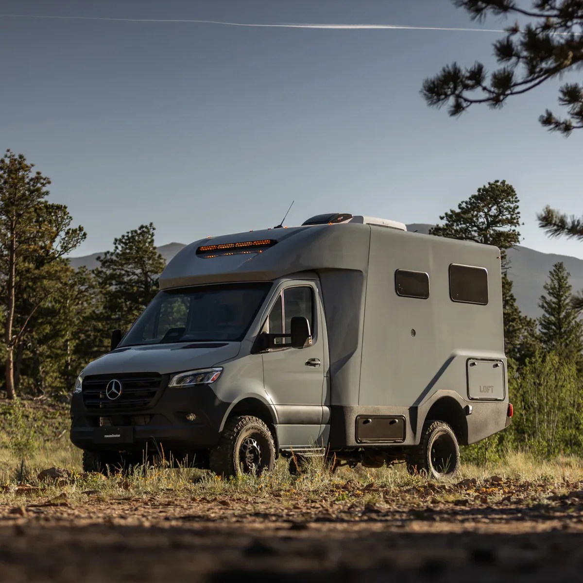Gray Mercedes-Benz camper van with off-road tires parked in a forest clearing.