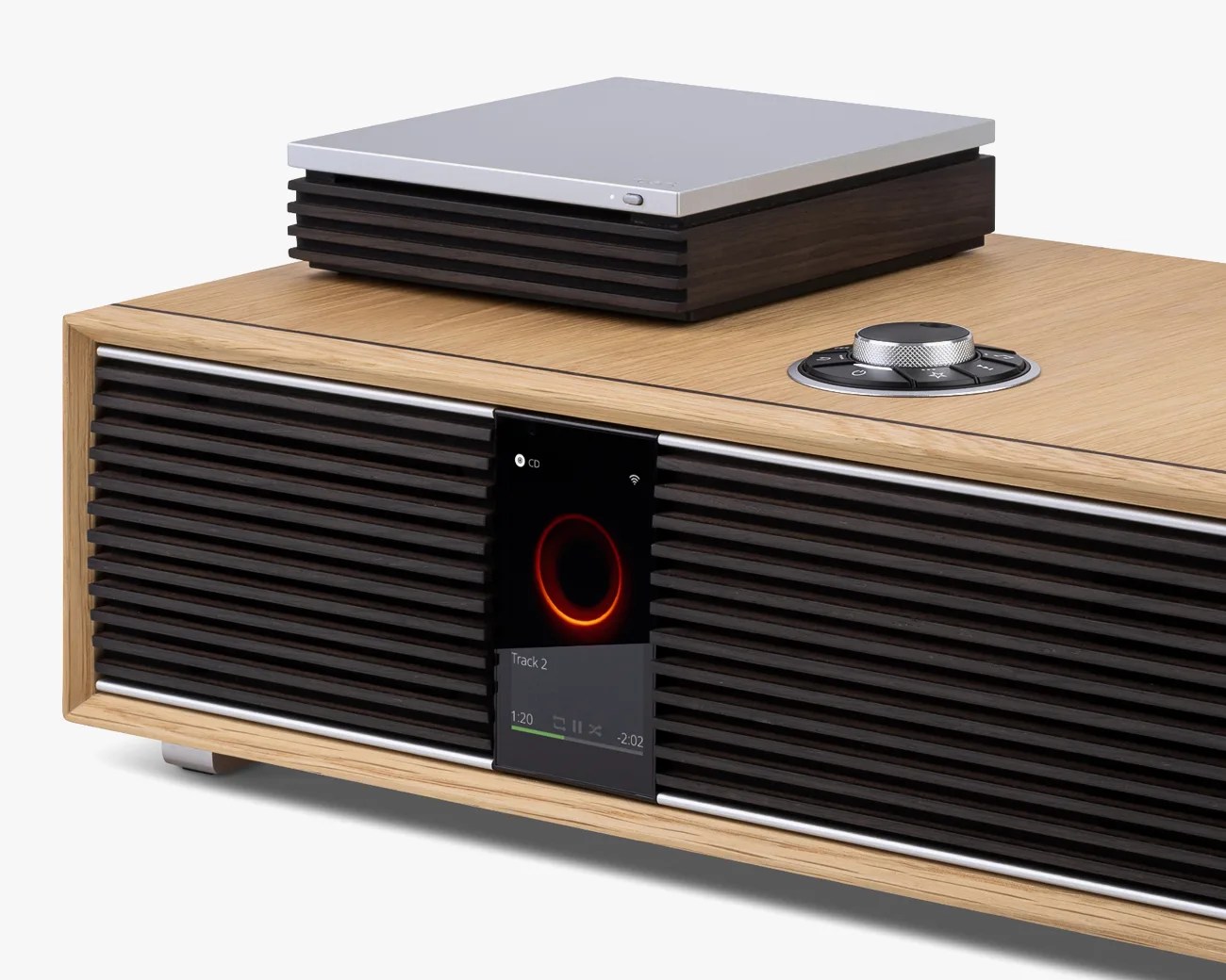 Wood-finished audio system with black horizontal speaker grills, a digital display, and a silver control knob on top.