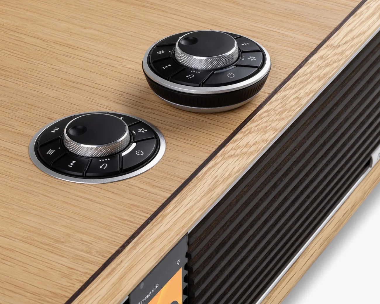 Close-up of a wooden speaker with two round black and silver control knobs, one recessed and one raised.