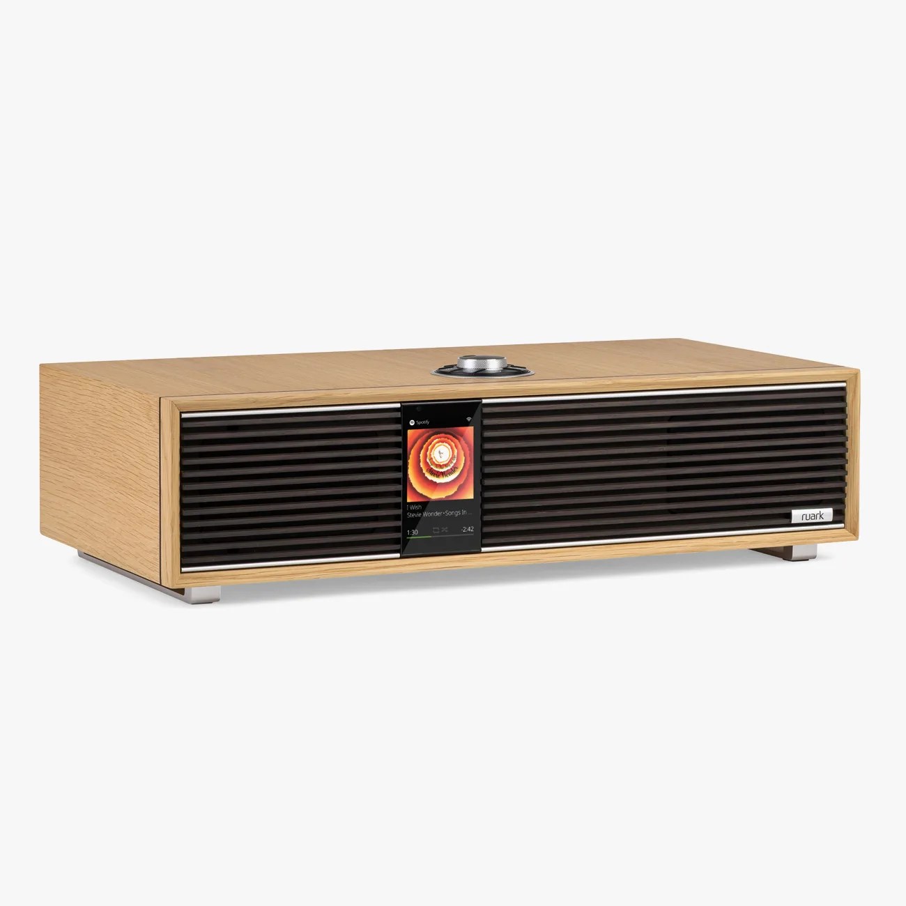 Rectangular wooden speaker with black front grille, central color display, and silver control knob on top.