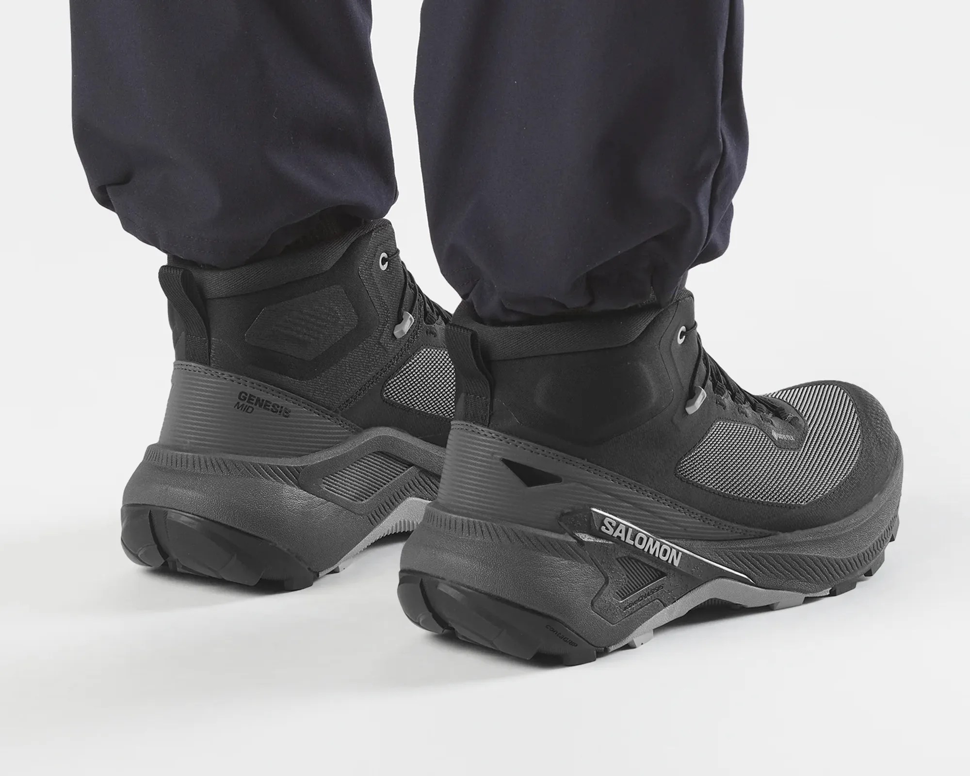 Black and gray Salomon Genesis Mid hiking boots worn with black pants.