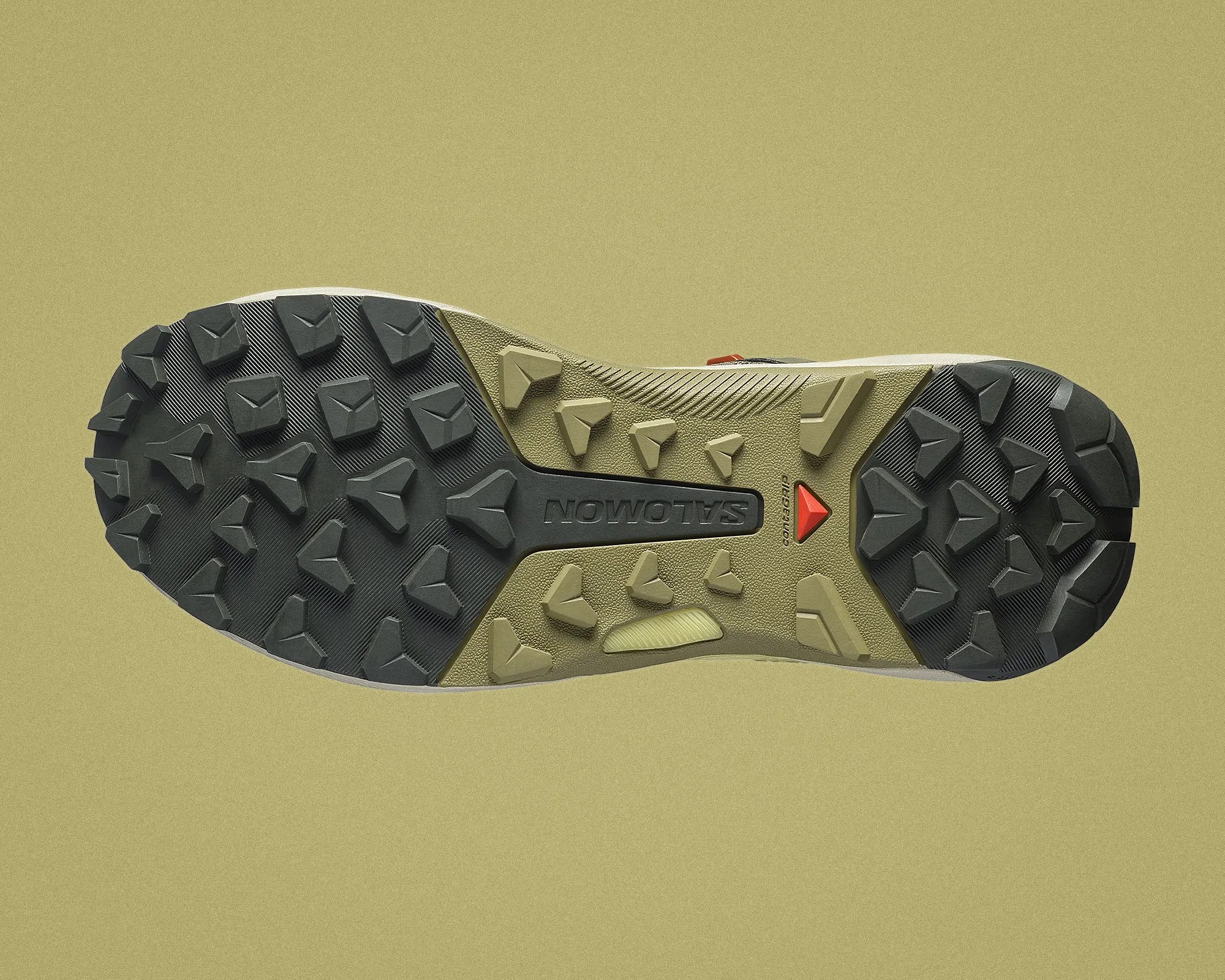 Close-up of a Salomon shoe sole with black and olive green aggressive tread lugs on a beige background.