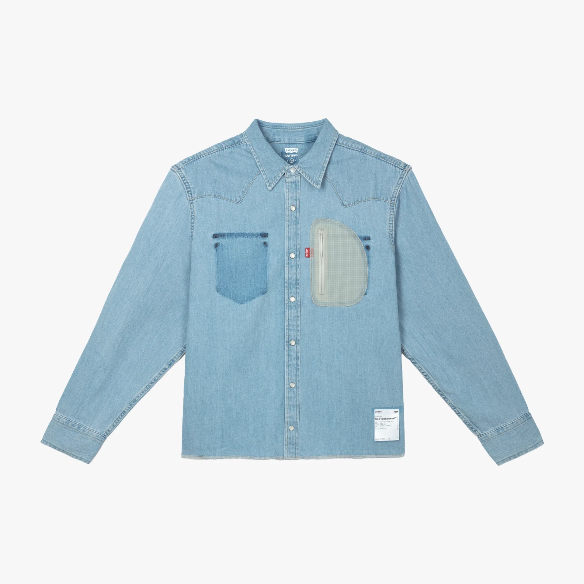 Light blue denim shirt with two chest pockets, one with a transparent zippered pouch and a white label near the hem.