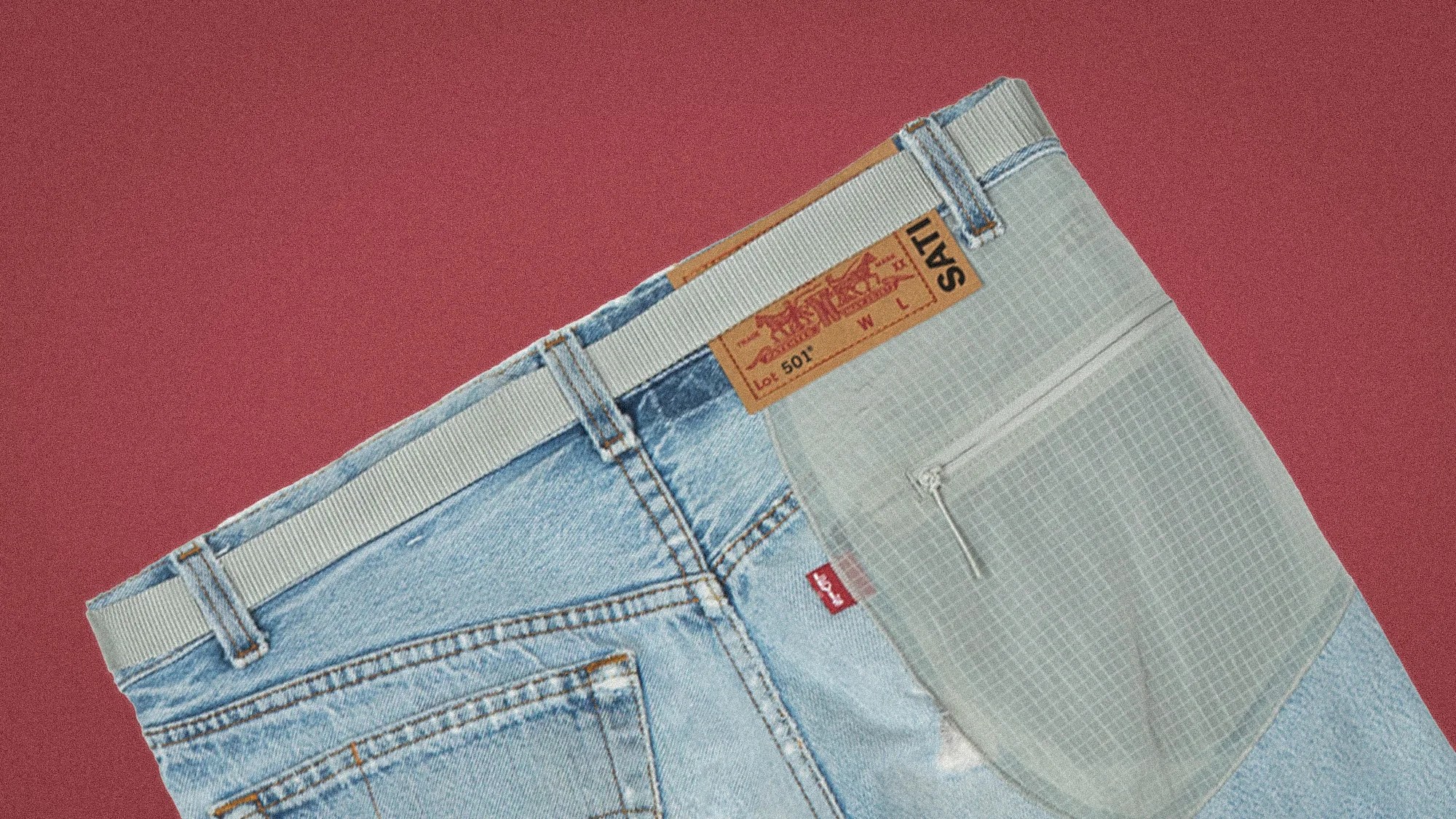 Light blue denim jeans with a gray fabric patch pocket and a white belt on a red background.