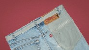 Light blue denim jeans with a gray fabric patch pocket and a white belt on a red background.
