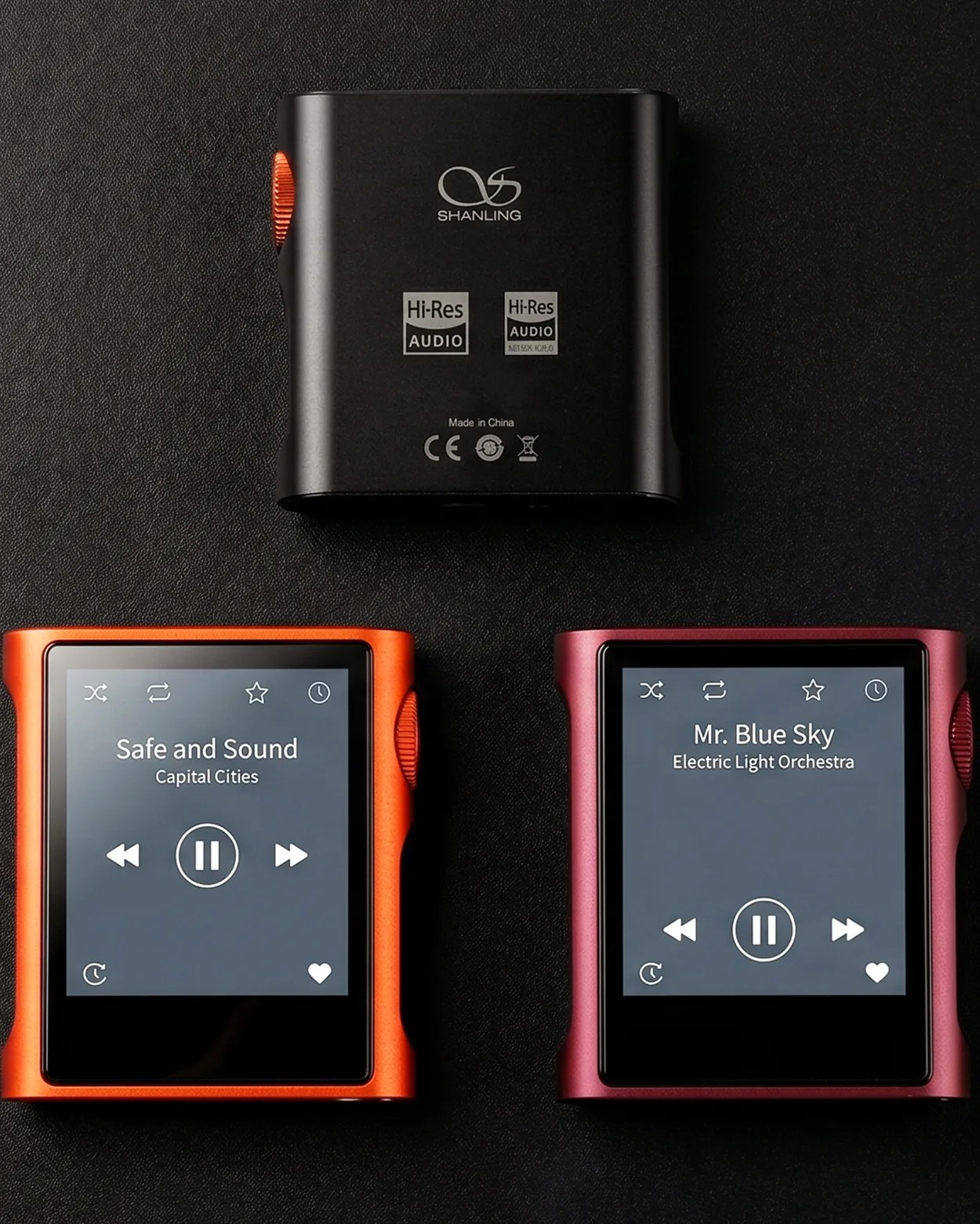 Three Shanling portable music players on a black surface, one black showing the back, one orange playing "Safe and Sound," and one red playing "Mr. Blue Sky.