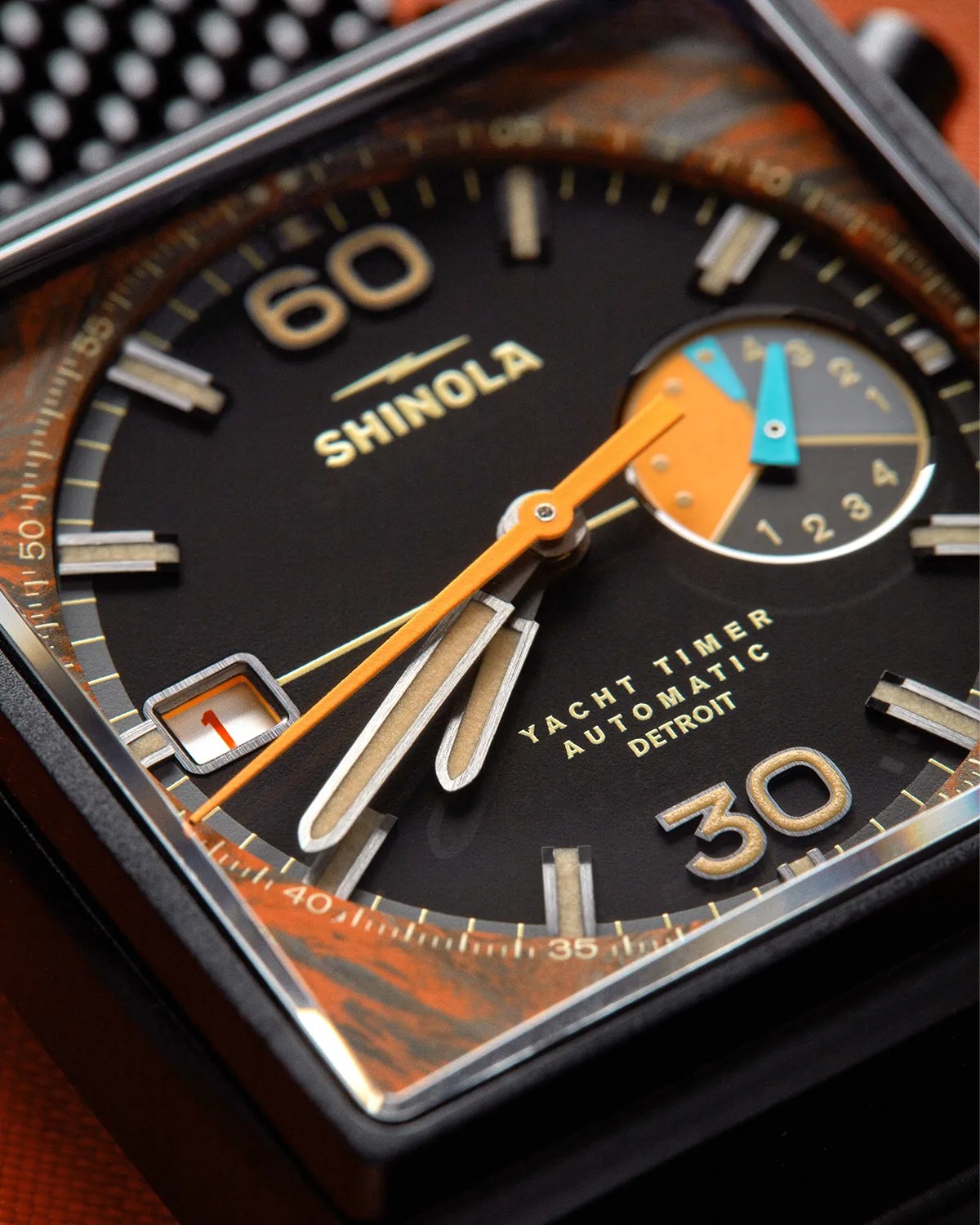 Close-up of a Shinola Yacht Timer Automatic watch face with black dial, orange and blue hands, and date window showing number 1.