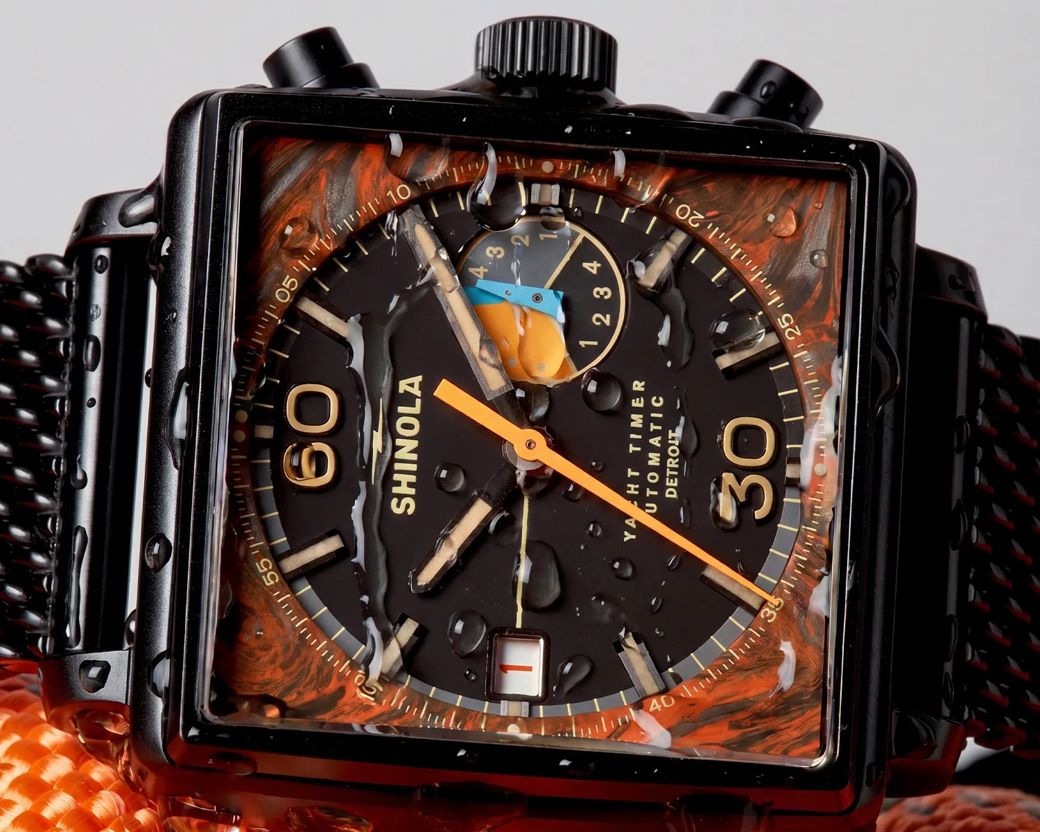 Close-up of a black Shinola Yacht Timer Automatic watch with orange and blue subdial hands and water droplets on the face.