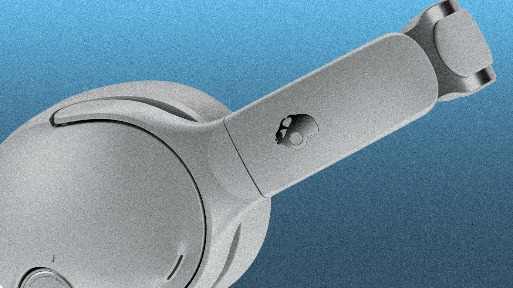 Close-up of gray Skullcandy over-ear headphone ear cup and headband against a blue background.