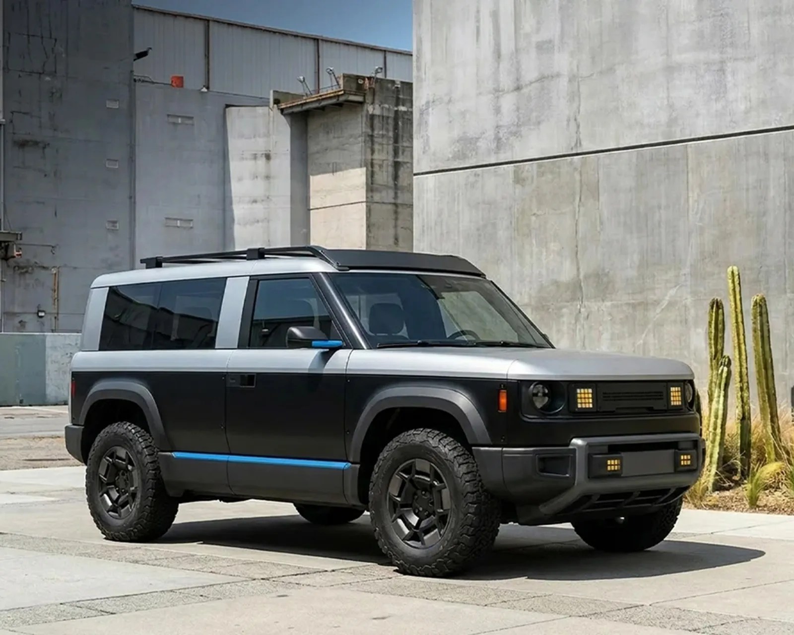 Black and silver electric SUV with off-road tires parked next to a concrete wall and cacti.