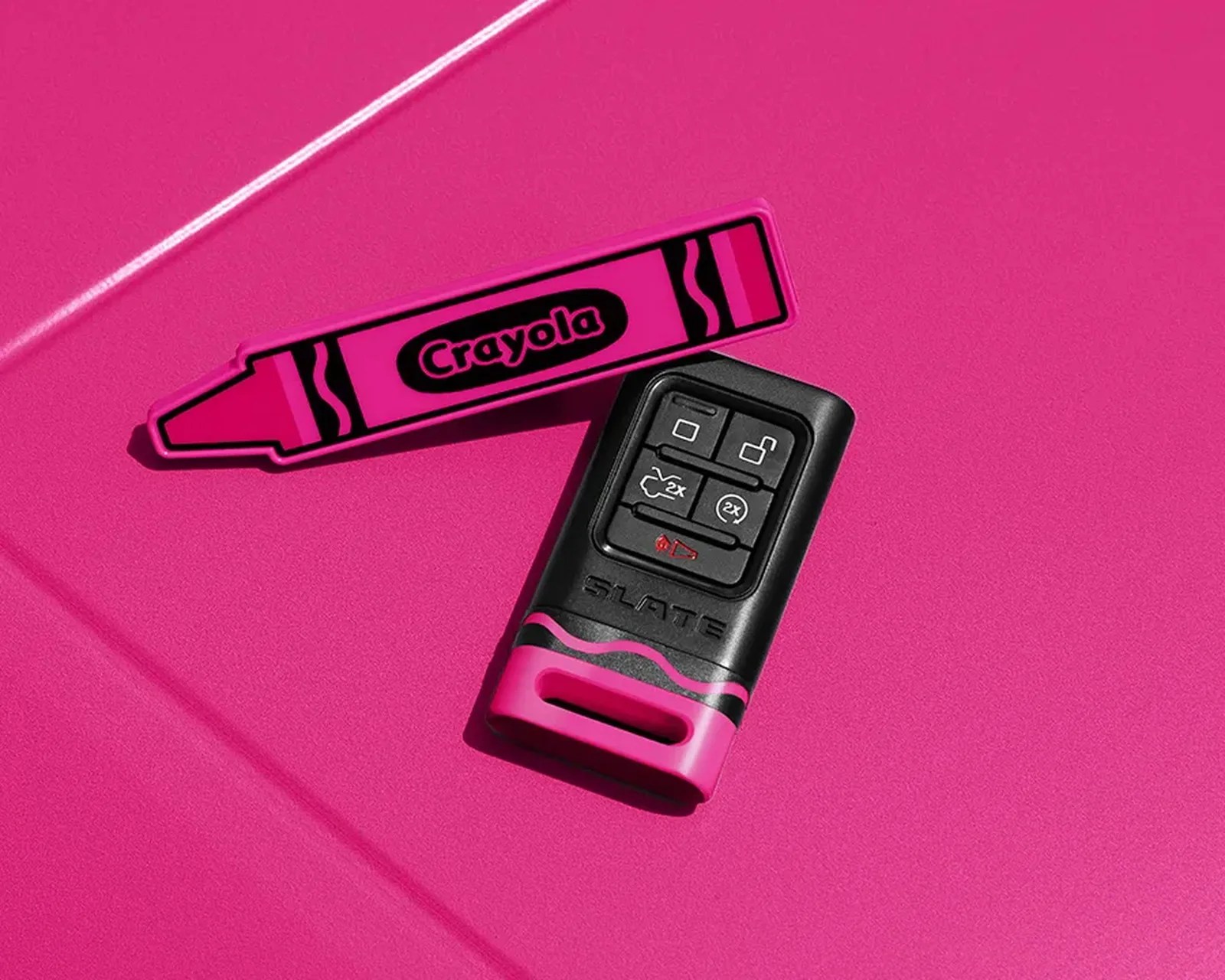 Black and pink Slate car key fob next to a pink Crayola crayon on a pink surface.