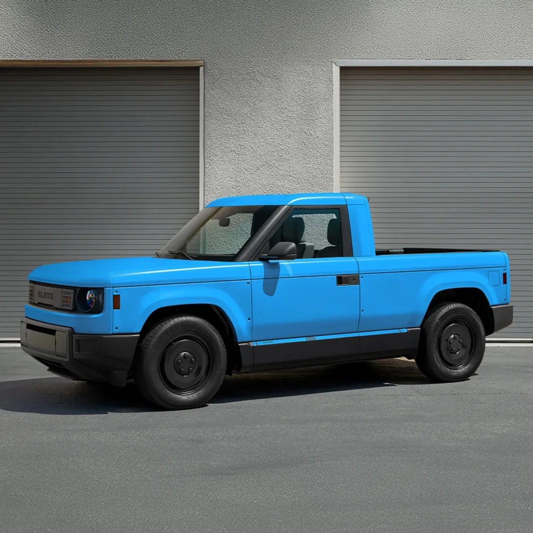 Bright blue compact electric pickup truck parked in front of gray garage doors.