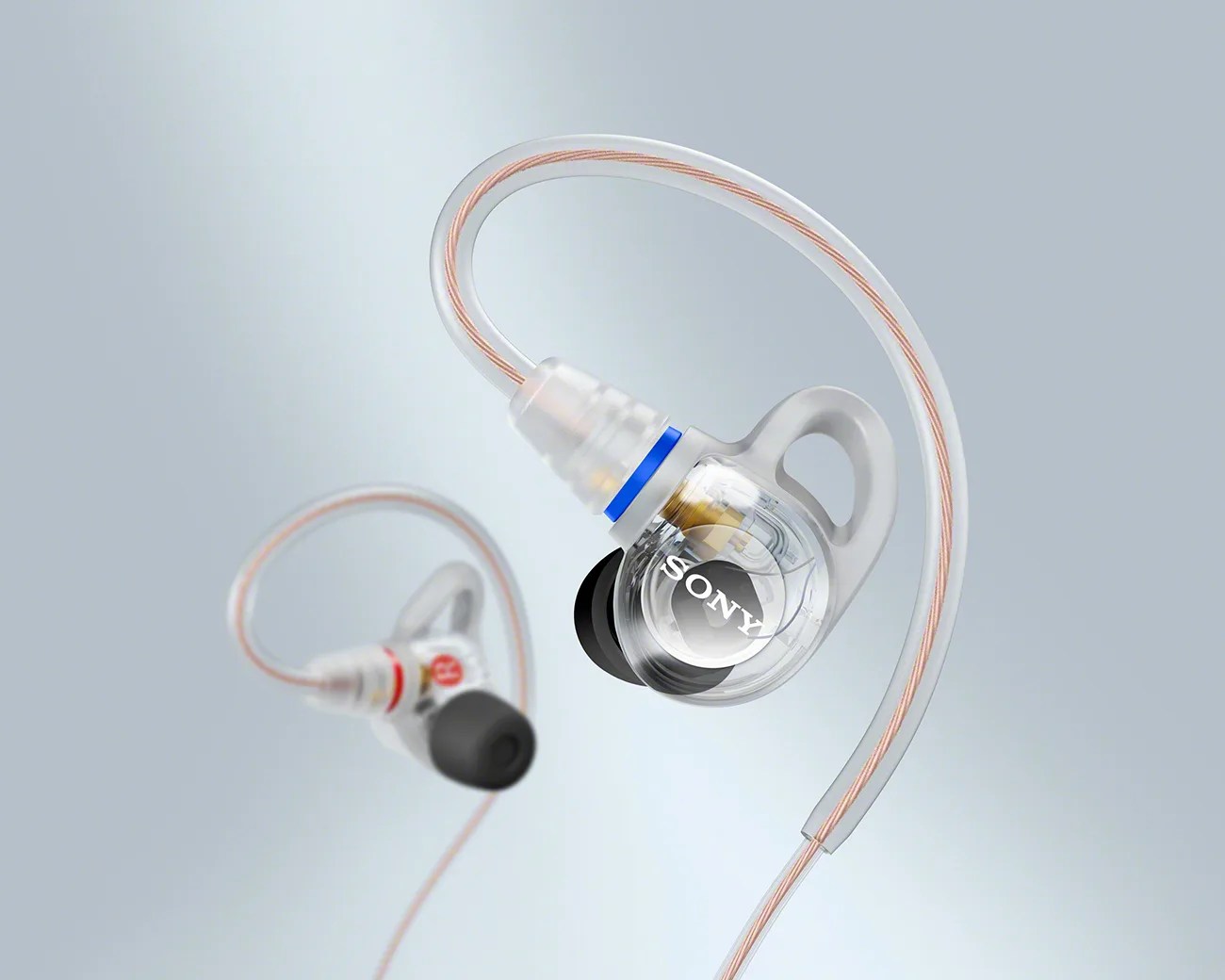 Transparent Sony in-ear headphones with over-ear hooks and copper-colored cables on a light gray background.