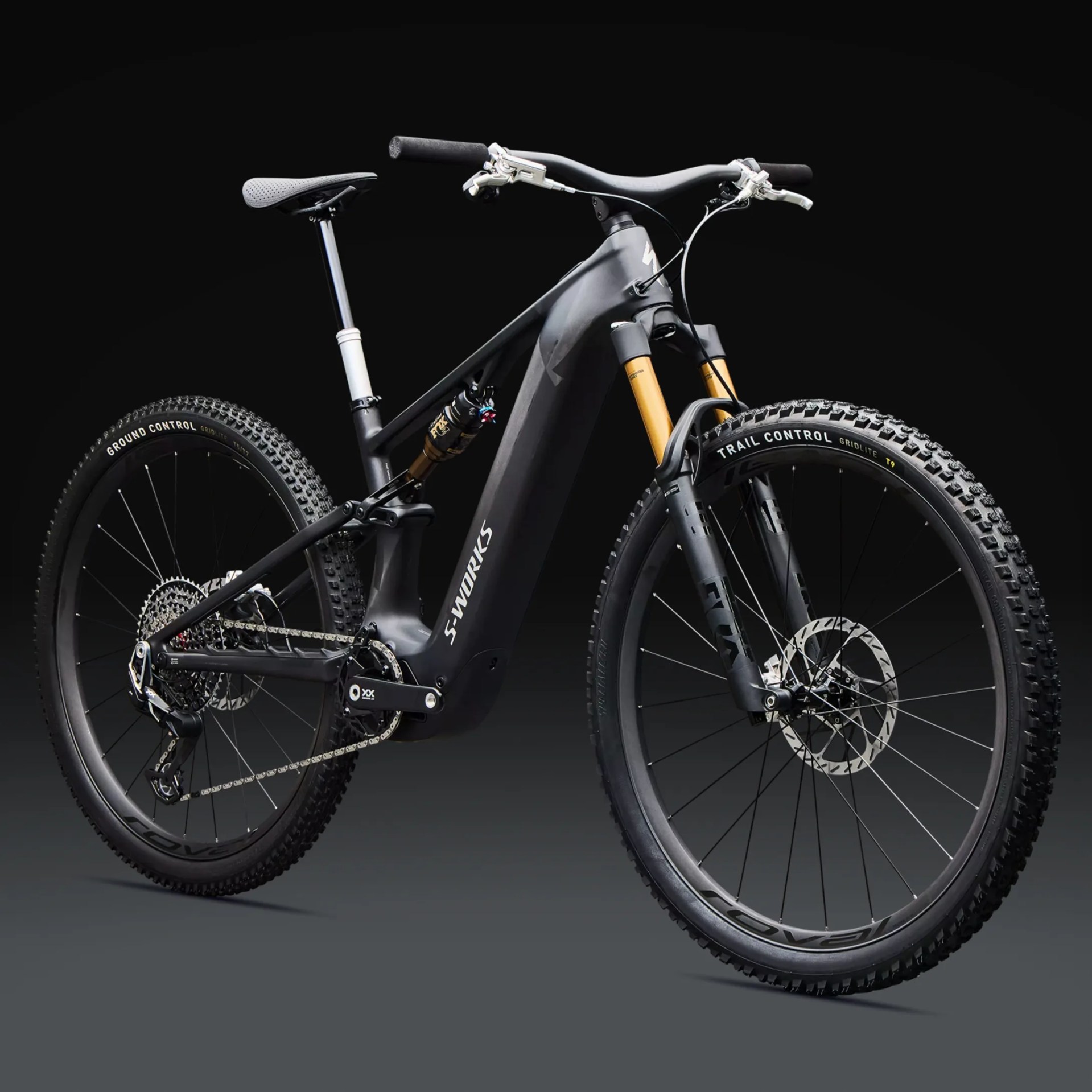Black Specialized S-Works mountain bike with gold suspension forks and knobby tires on a dark background.