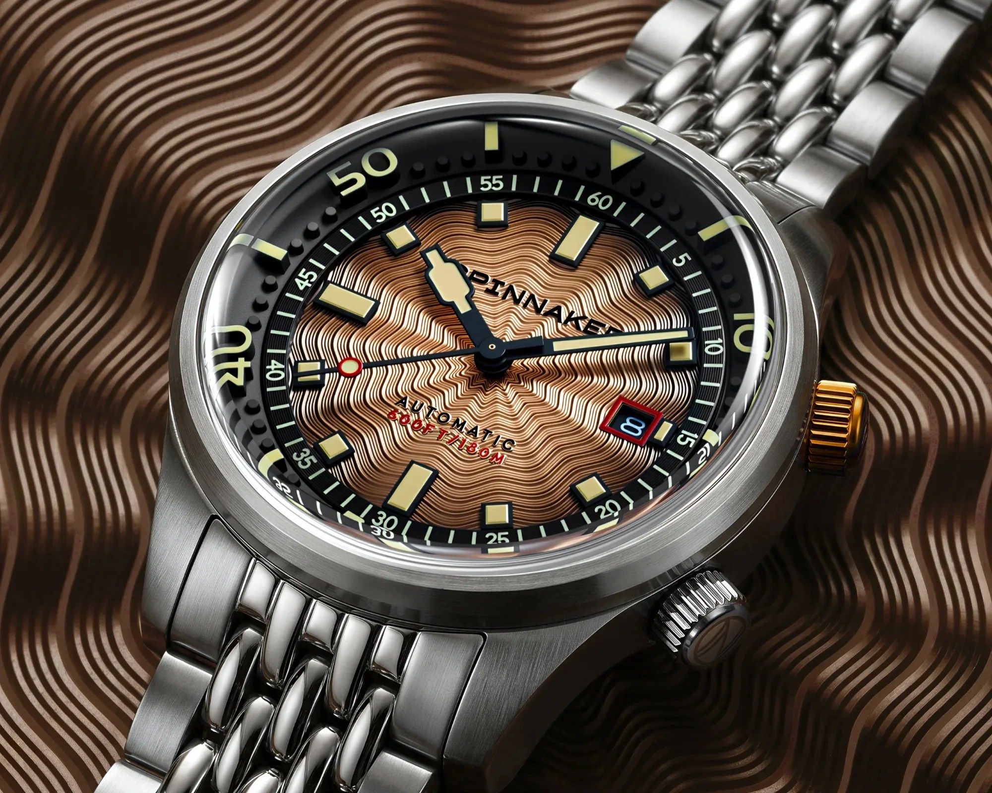 Close-up of a stainless steel wristwatch with a textured bronze dial, luminous markers, and a date window showing the number 8.