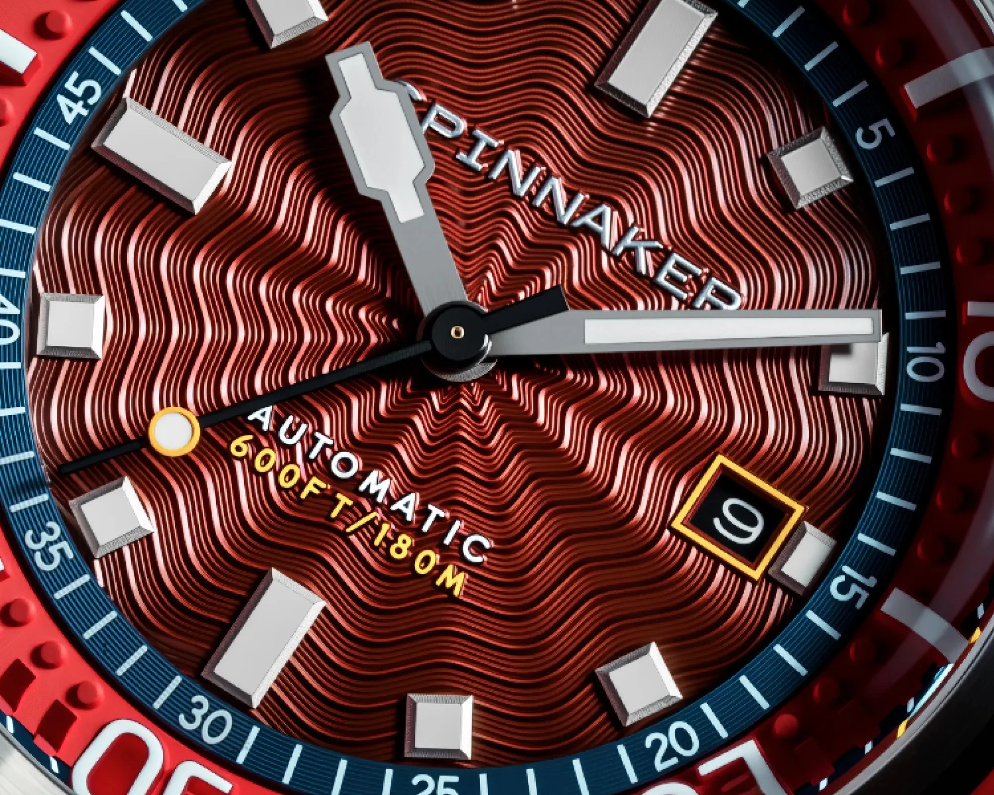Close-up of a red textured watch dial with silver rectangular hour markers, white hands, and a date window showing the number 9.