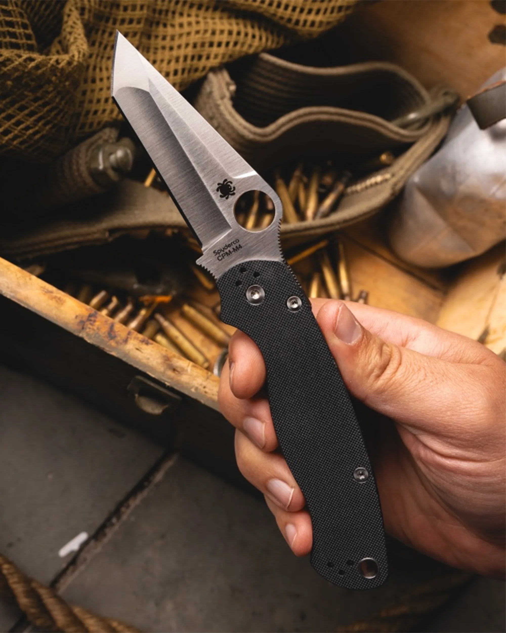 Hand holding a Spyderco CPM-M4 folding knife with a black textured handle and partially serrated blade.