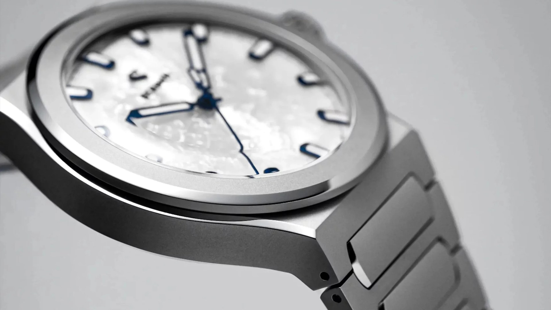 Close-up of a silver metal wristwatch with a textured white dial and blue hour markers and hands.