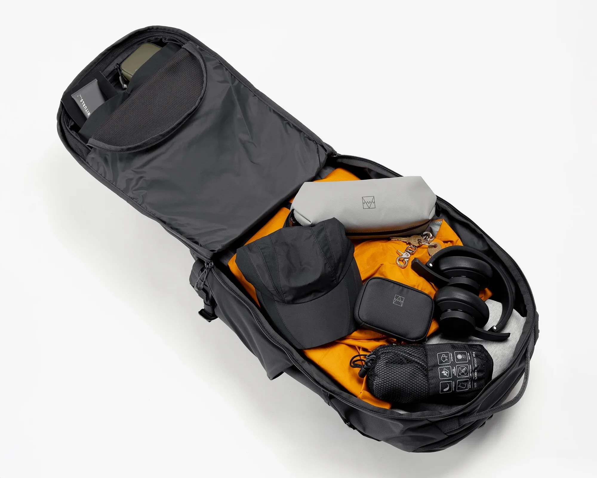 Black travel backpack open with orange jacket, black cap, gray pouch, black headphones, and small black bags inside.