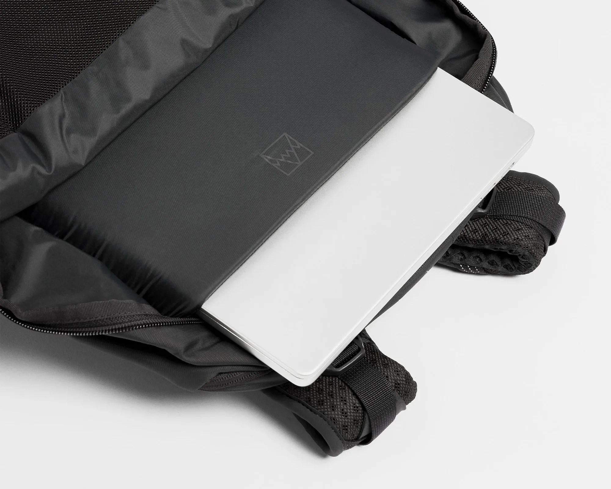 Black padded laptop sleeve inside an open black backpack with mesh straps, holding a silver laptop.