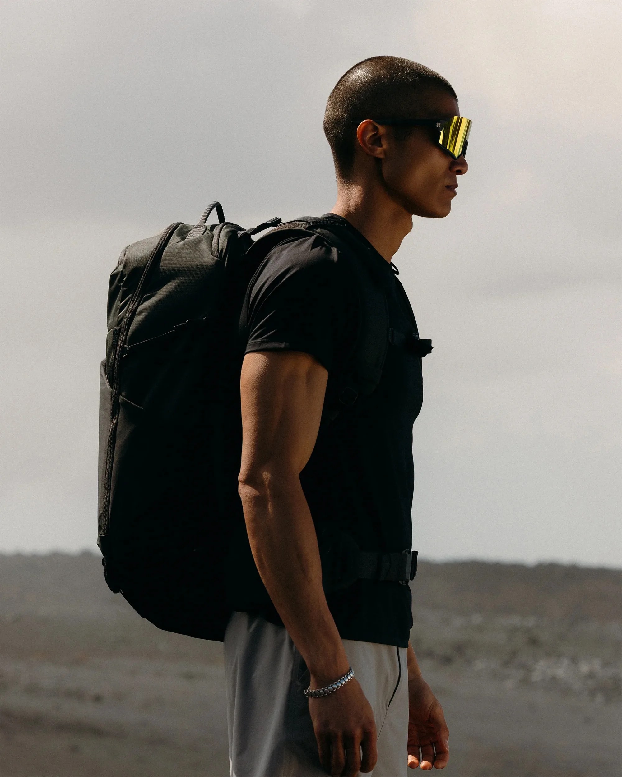 Man wearing black shirt and gray pants with a large black backpack and reflective yellow sunglasses.